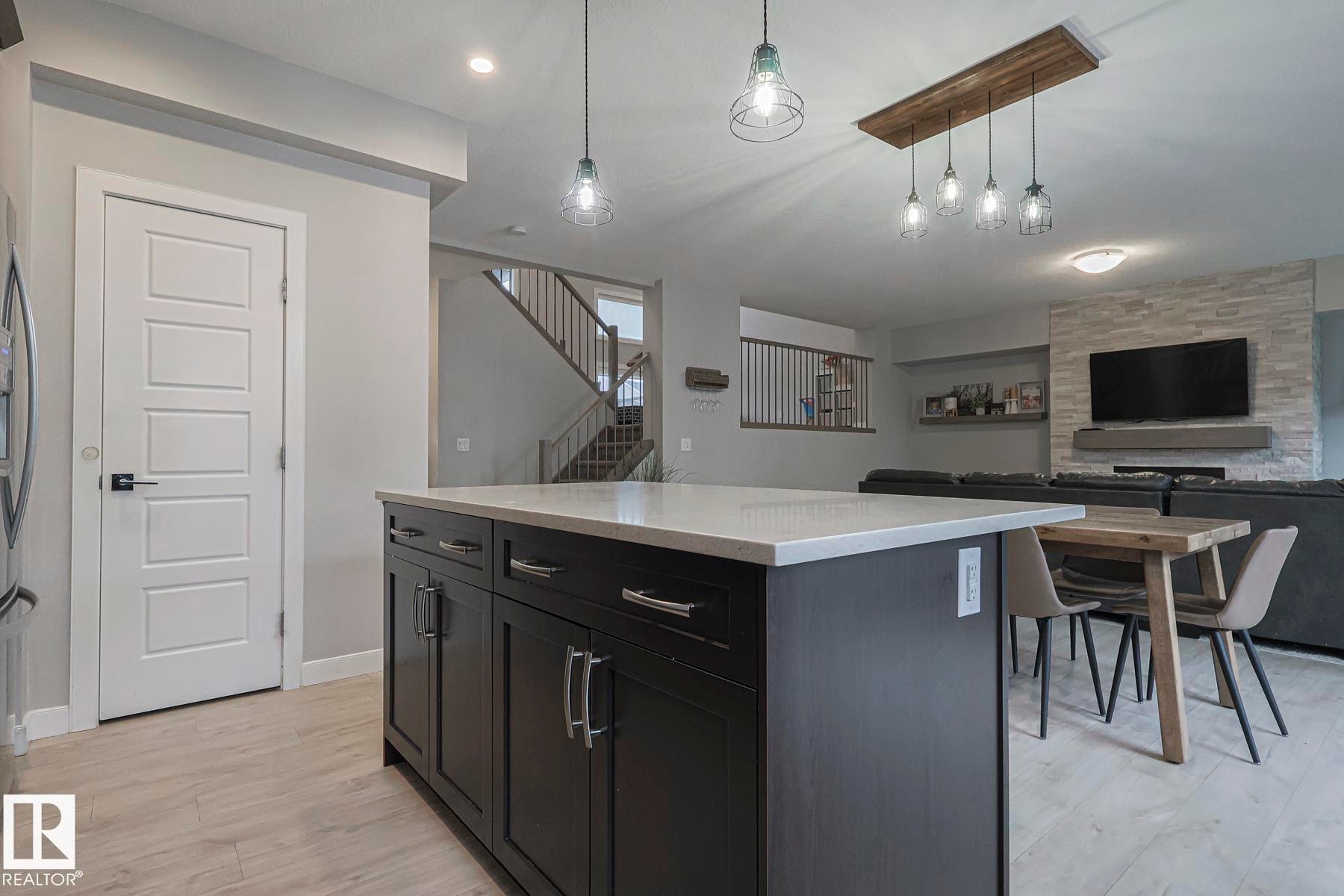 Kitchen featuring open floor plan, a kitchen island, pendant lighting, light wood-style floors, and light stone counters - 2011 201 Street, Edmonton, AB - Indoor