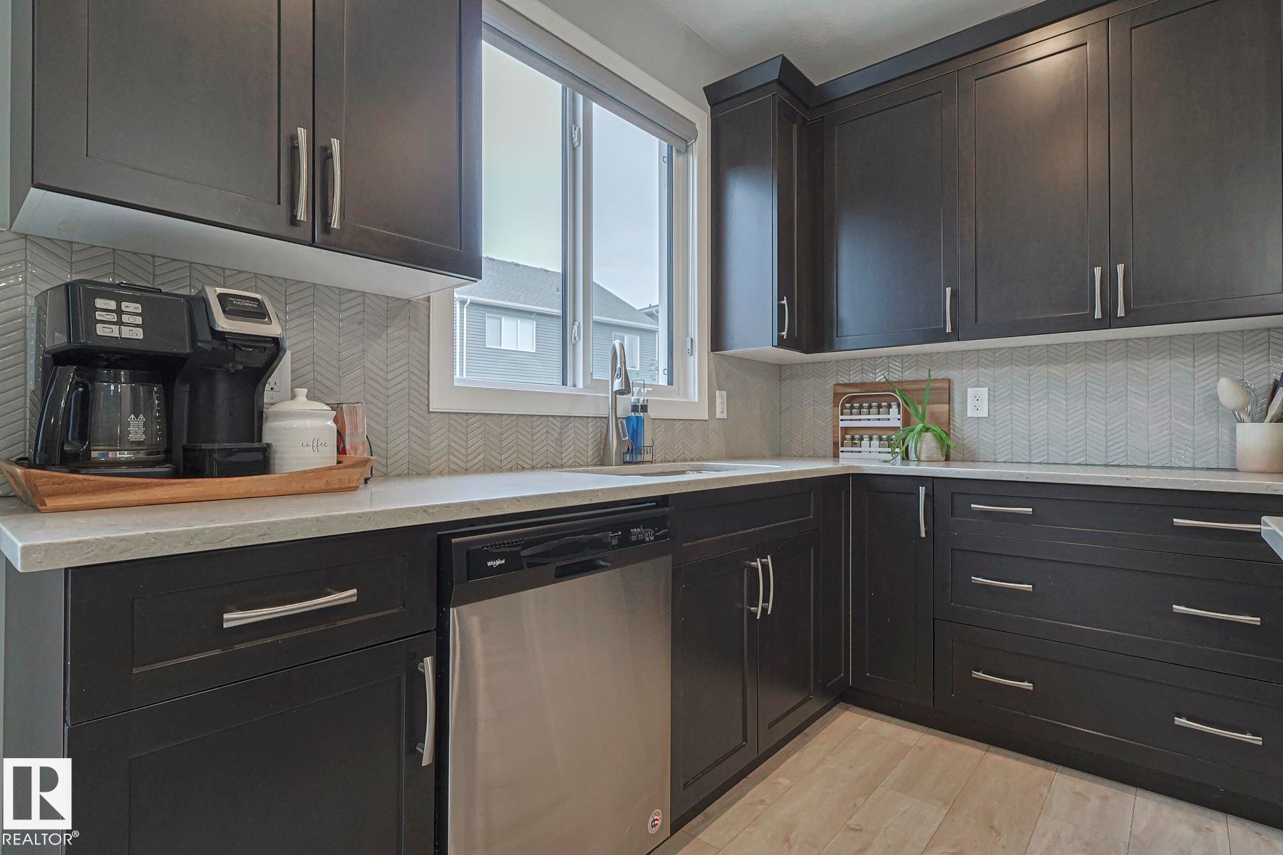 Kitchen with backsplash, stainless steel dishwasher, light wood-type flooring, light stone counters, and dark cabinets - 2011 201 Street, Edmonton, AB - Indoor Photo Showing Kitchen