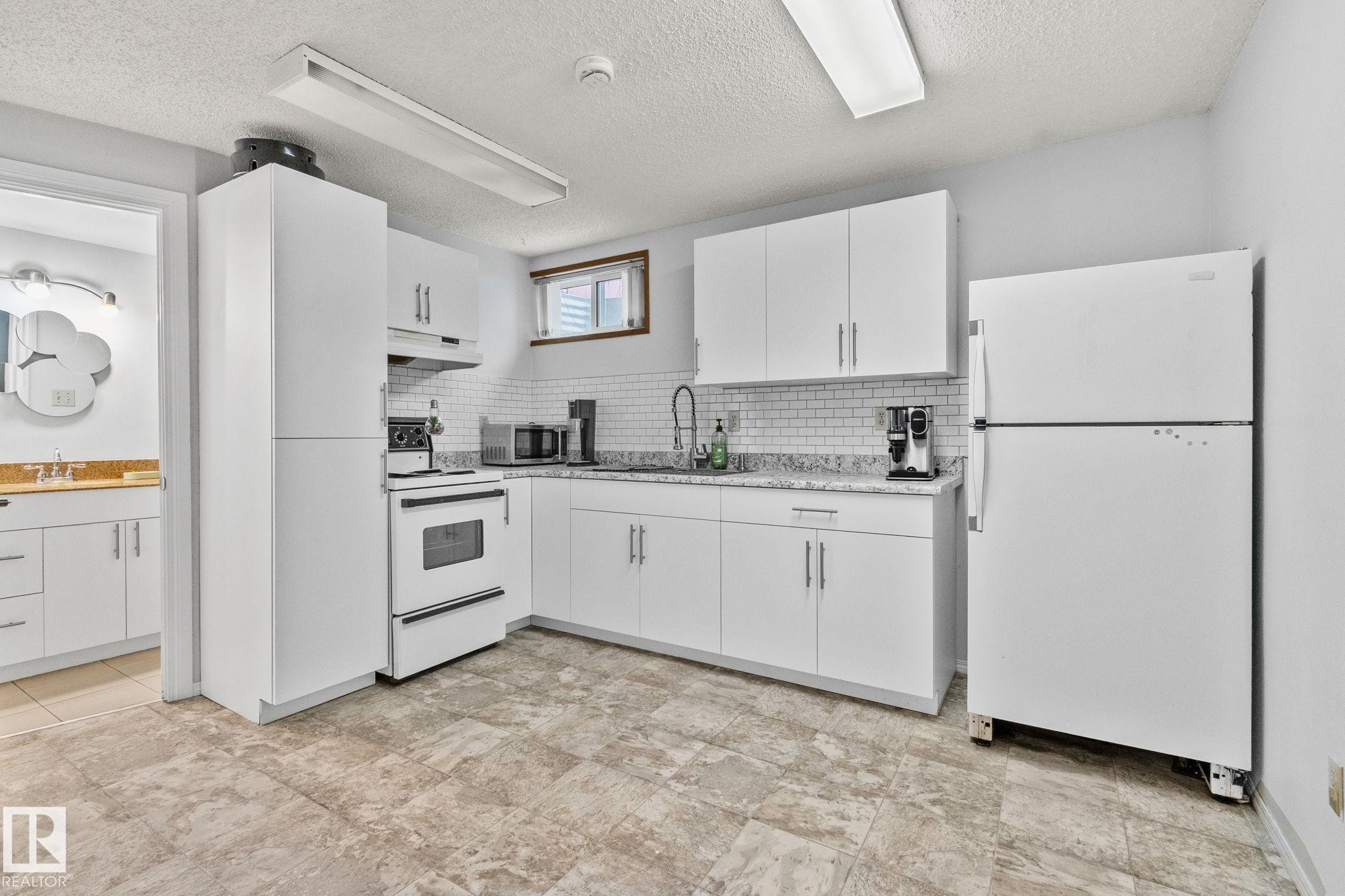 Kitchen featuring white appliances, white cabinets, under cabinet range hood, decorative backsplash, and a textured ceiling - 17523 95 Street, Edmonton, AB - Indoor Photo Showing Kitchen