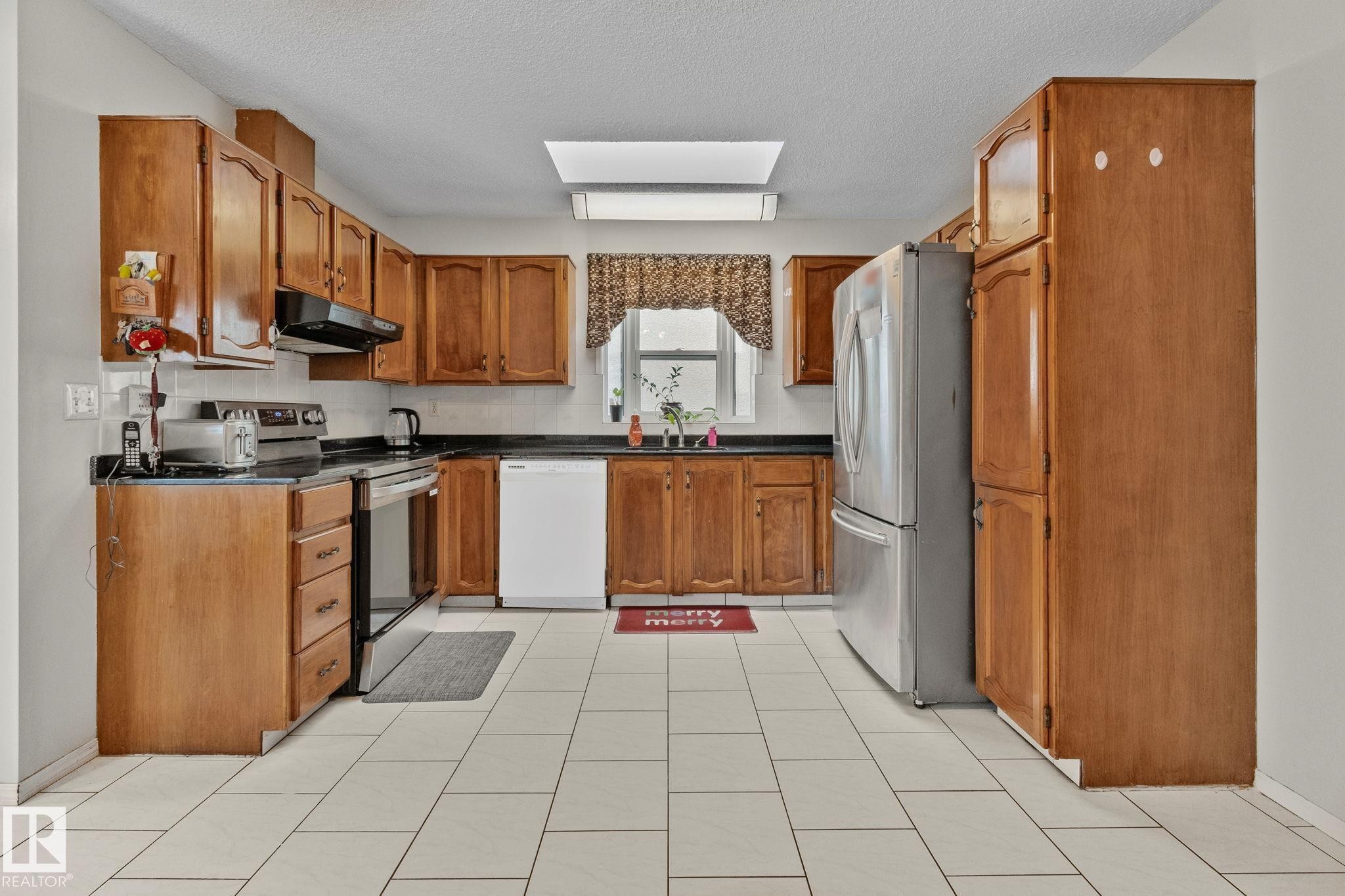 Kitchen with brown cabinets, stainless steel appliances, a skylight, a textured ceiling, and under cabinet range hood - 17523 95 Street, Edmonton, AB - Indoor Photo Showing Kitchen