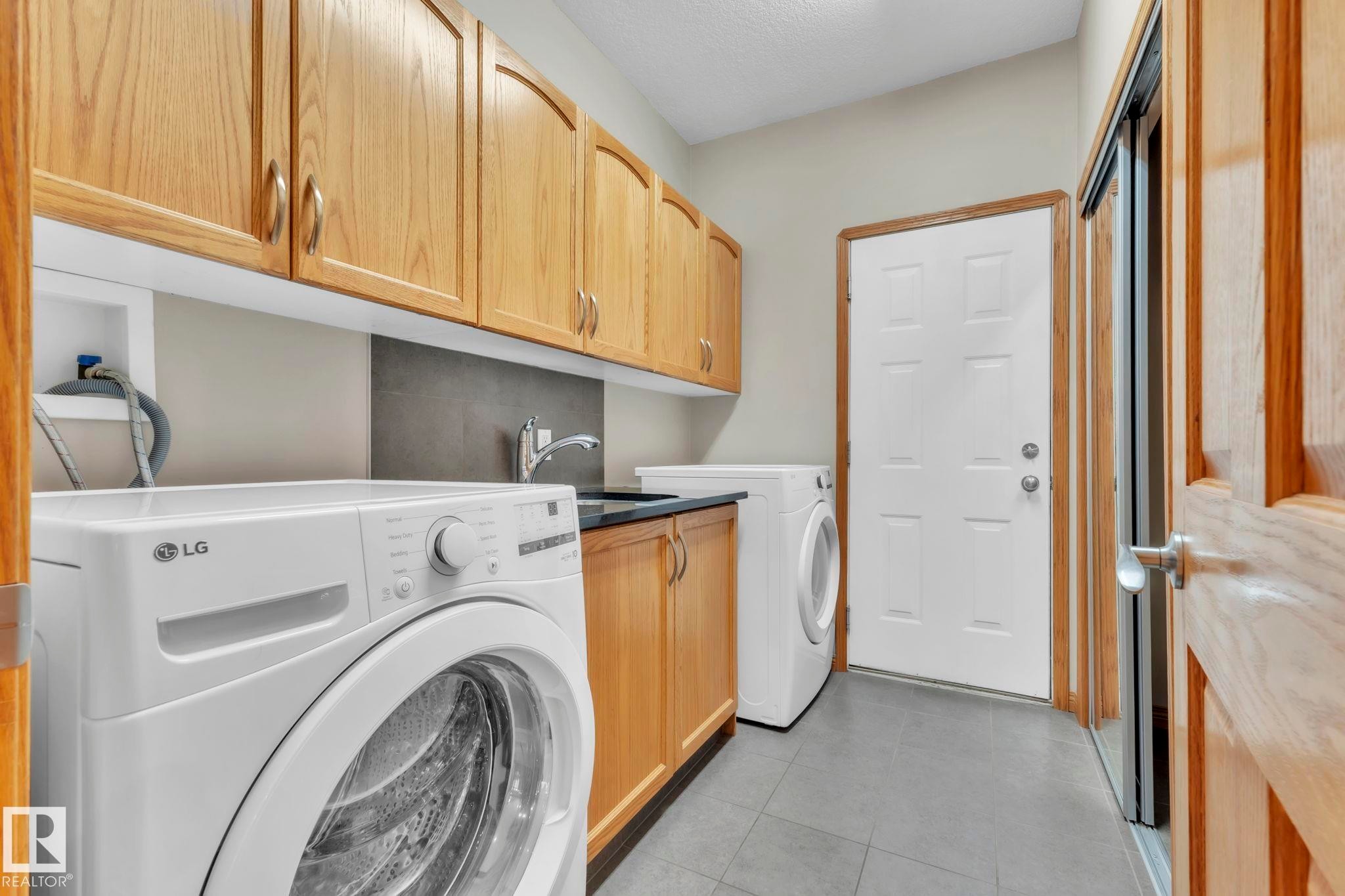 Washroom featuring cabinet space, light tile patterned floors, and washing machine and dryer - 1217 Summerside Drive, Edmonton, AB - Indoor Photo Showing Laundry Room