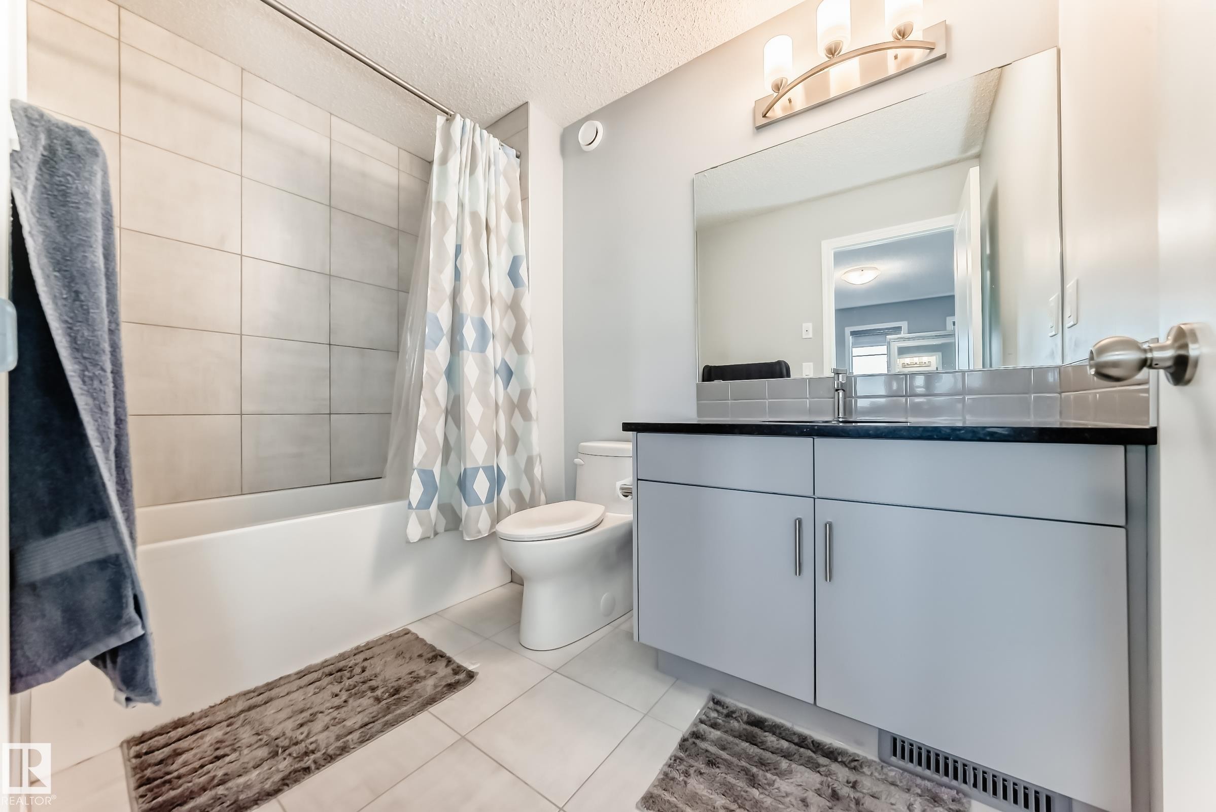 Full bathroom featuring vanity, light tile patterned floors, a textured ceiling, and shower / bath combination with curtain - 1002 Stillwater Boulevard, Edmonton, AB - Indoor Photo Showing Bathroom