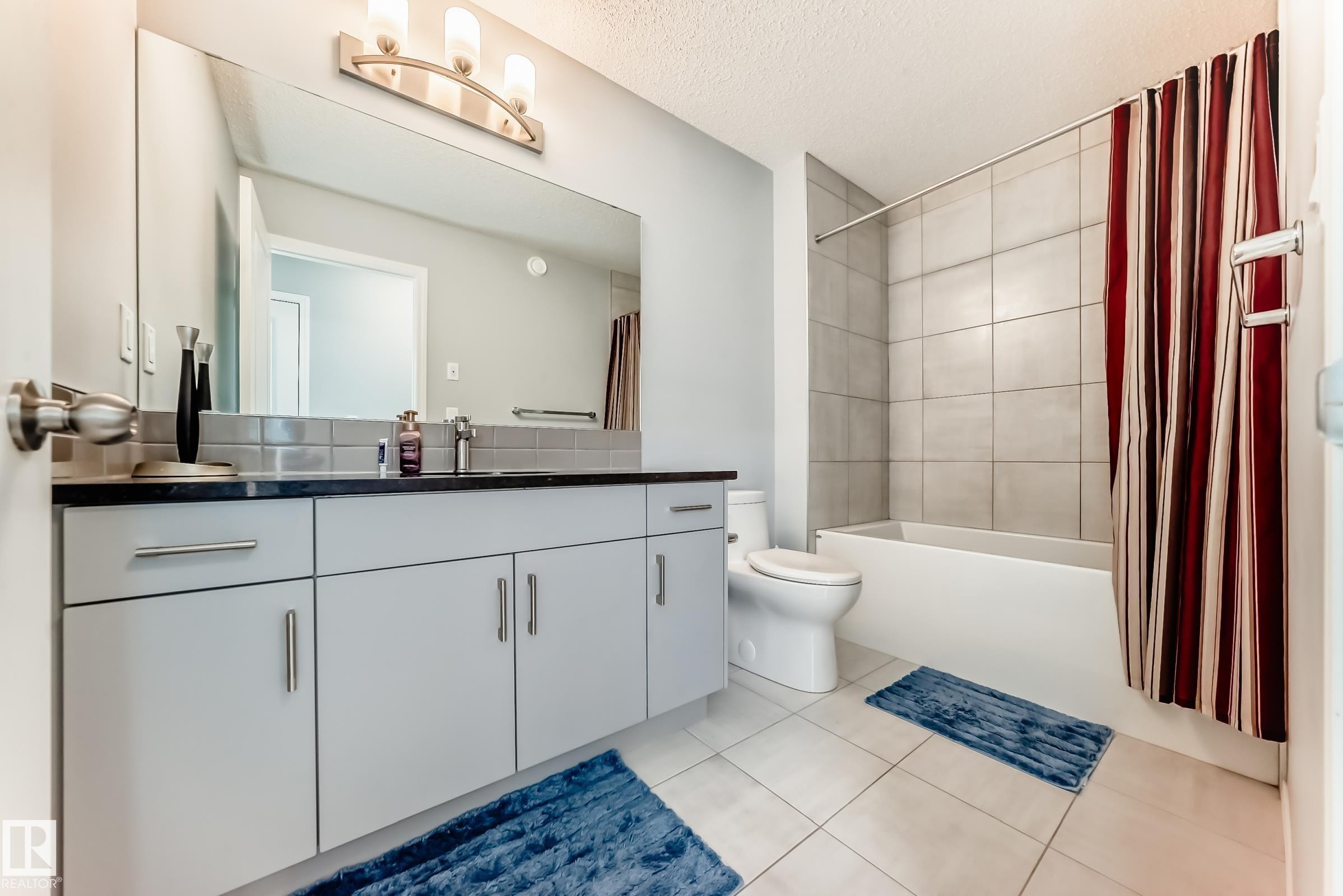 Bathroom with vanity, shower / bathtub combination with curtain, light tile patterned floors, and a textured ceiling - 1002 Stillwater Boulevard, Edmonton, AB - Indoor Photo Showing Bathroom