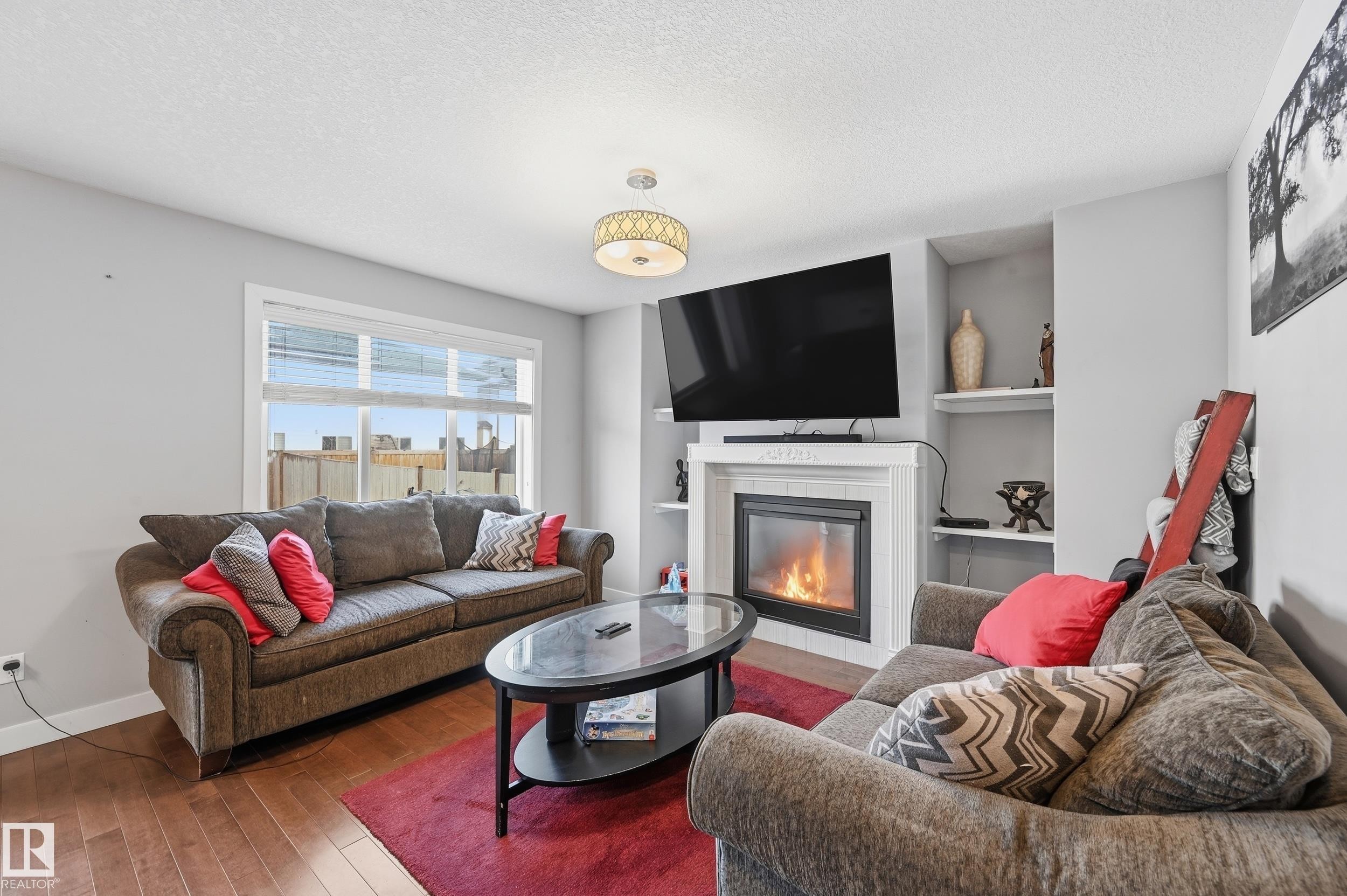 Living area featuring a tiled fireplace, a textured ceiling, and wood-type flooring - 5978 167C Avenue, Edmonton, AB - Indoor Photo Showing Living Room With Fireplace