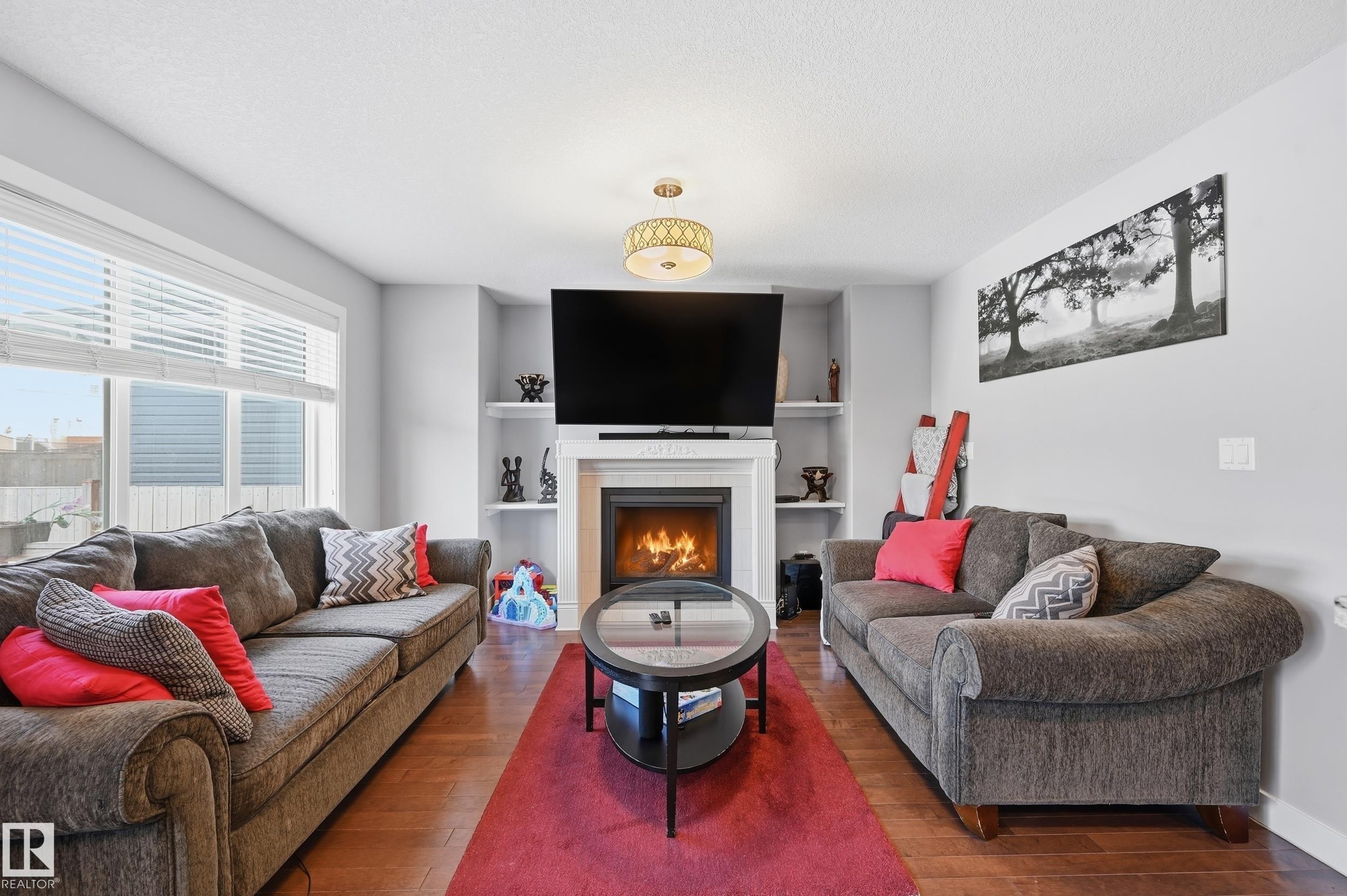 Living area featuring a tile fireplace, hardwood / wood-style flooring, built in features, and a textured ceiling - 5978 167C Avenue, Edmonton, AB - Indoor Photo Showing Living Room With Fireplace