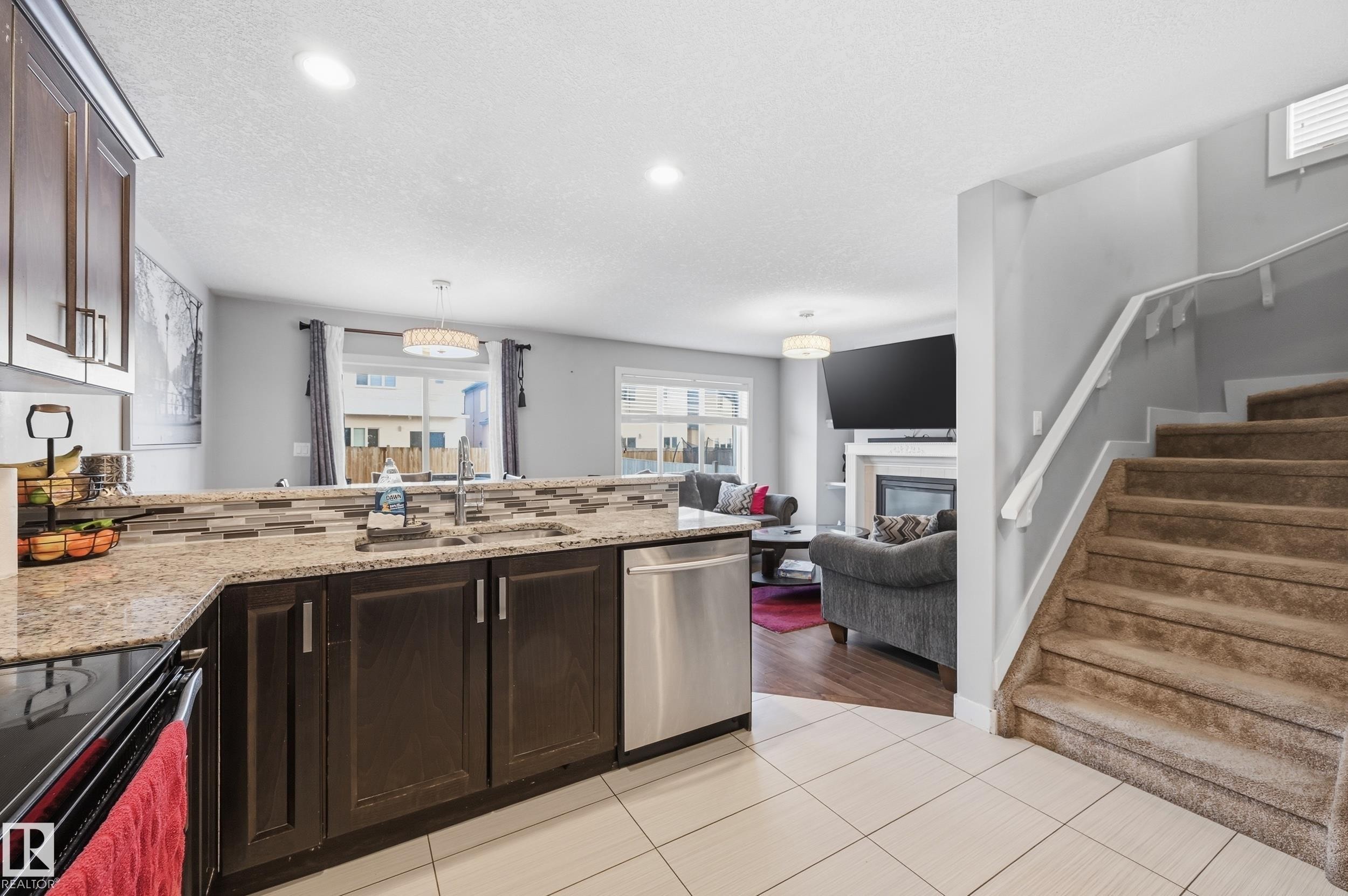 Kitchen featuring a peninsula, dark wood finish cabinets, electric stove, light stone counters, and a textured ceiling - 5978 167C Avenue, Edmonton, AB - Indoor Photo Showing Kitchen With Fireplace With Upgraded Kitchen