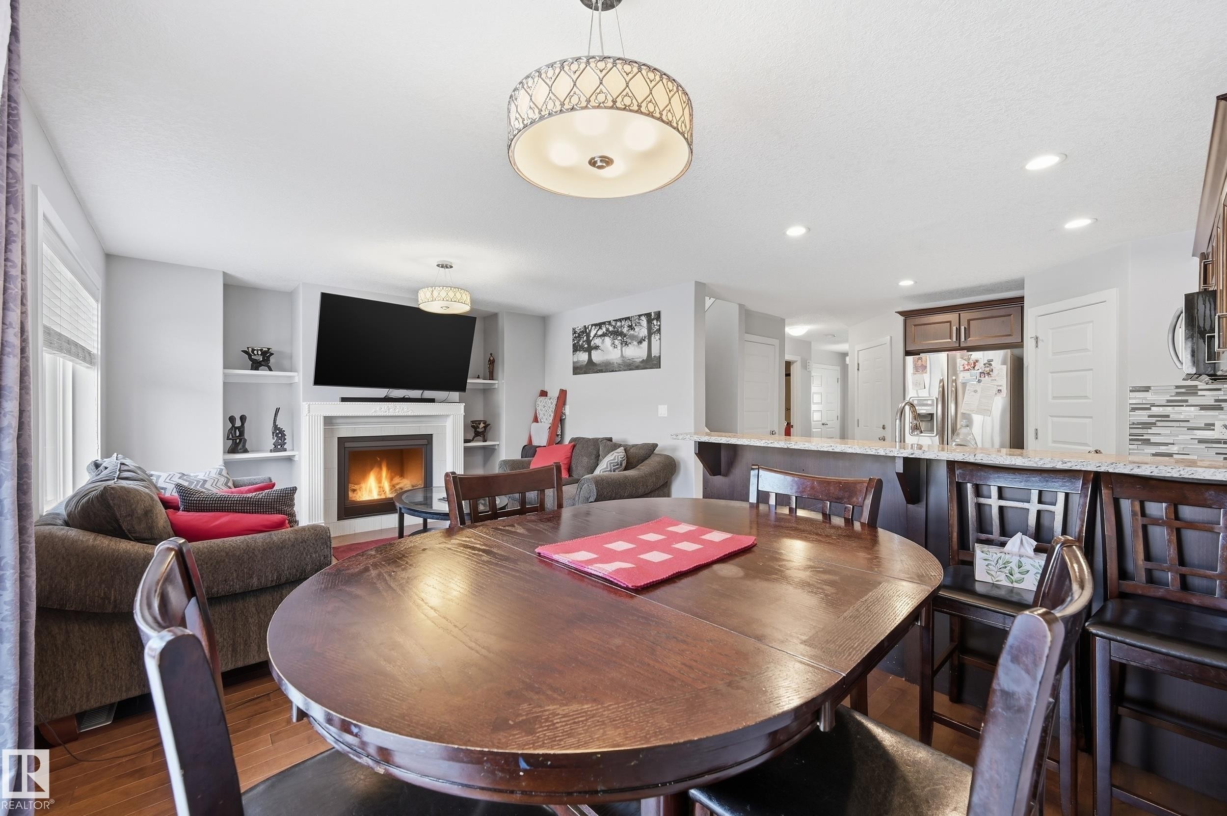 Dining space with wood finished floors, a lit fireplace, recessed lighting, and built in features - 5978 167C Avenue, Edmonton, AB - Indoor Photo Showing Dining Room With Fireplace