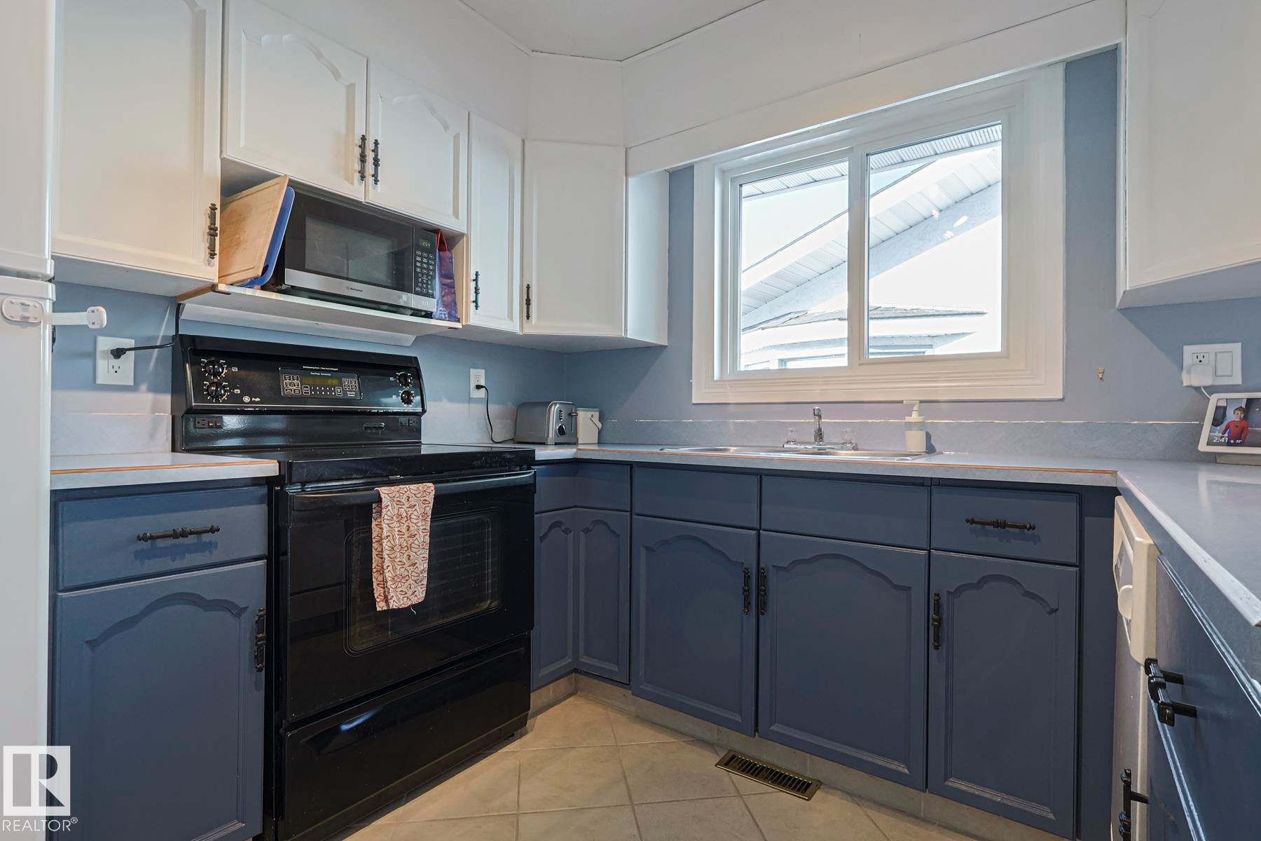 Two tone kitchen with black / electric stove, light countertops, two tone color scheme, stainless steel microwave, and light tile patterned floors - 192 Dunluce Road, Edmonton, AB - Indoor Photo Showing Kitchen