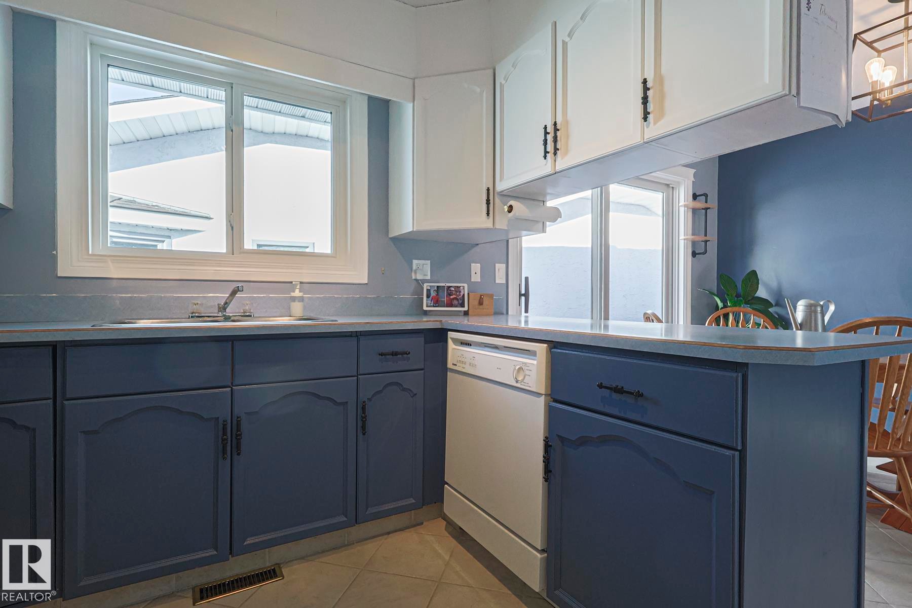 Kitchen with dishwasher, a peninsula, light tile patterned floors, healthy amount of natural light, and two tone cabinetry - 192 Dunluce Road, Edmonton, AB - Indoor Photo Showing Kitchen With Double Sink