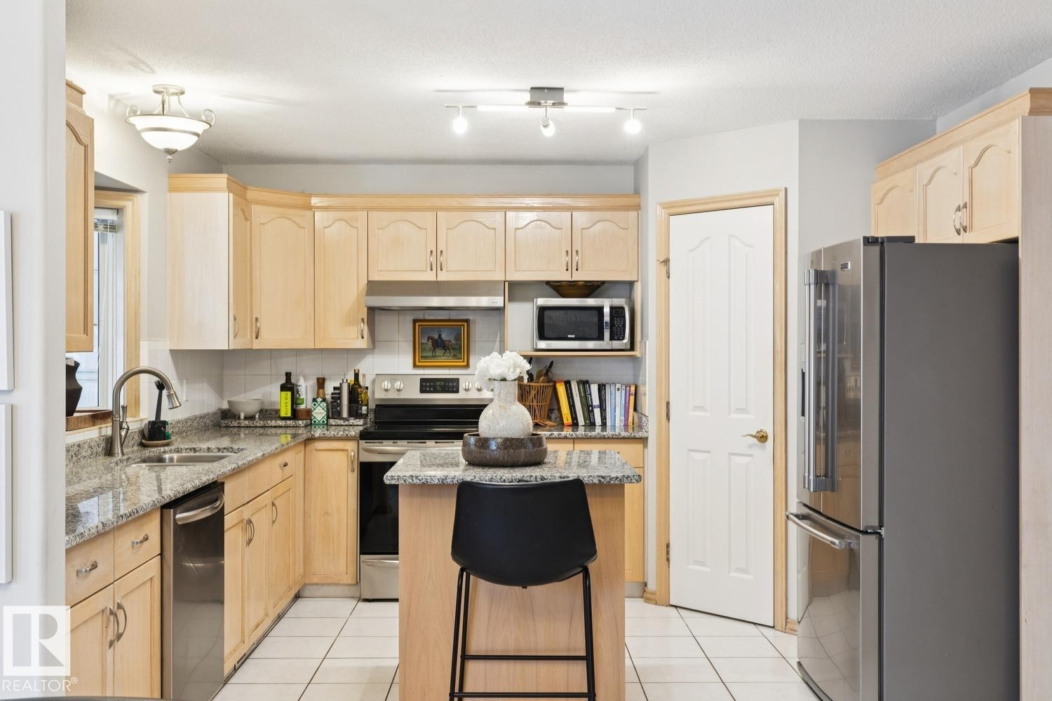 Kitchen featuring light brown cabinetry, appliances with stainless steel finishes, light stone countertops, a kitchen island, and light tile patterned floors - 8617 158A Avenue, Edmonton, AB - Indoor Photo Showing Kitchen