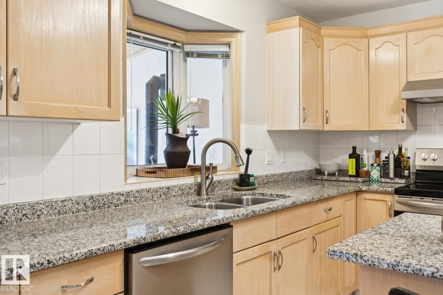 Kitchen with light brown cabinetry, tasteful backsplash, light stone countertops, appliances with stainless steel finishes, and under cabinet range hood - 8617 158A Avenue, Edmonton, AB - Indoor Photo Showing Kitchen With Double Sink With Upgraded Kitchen