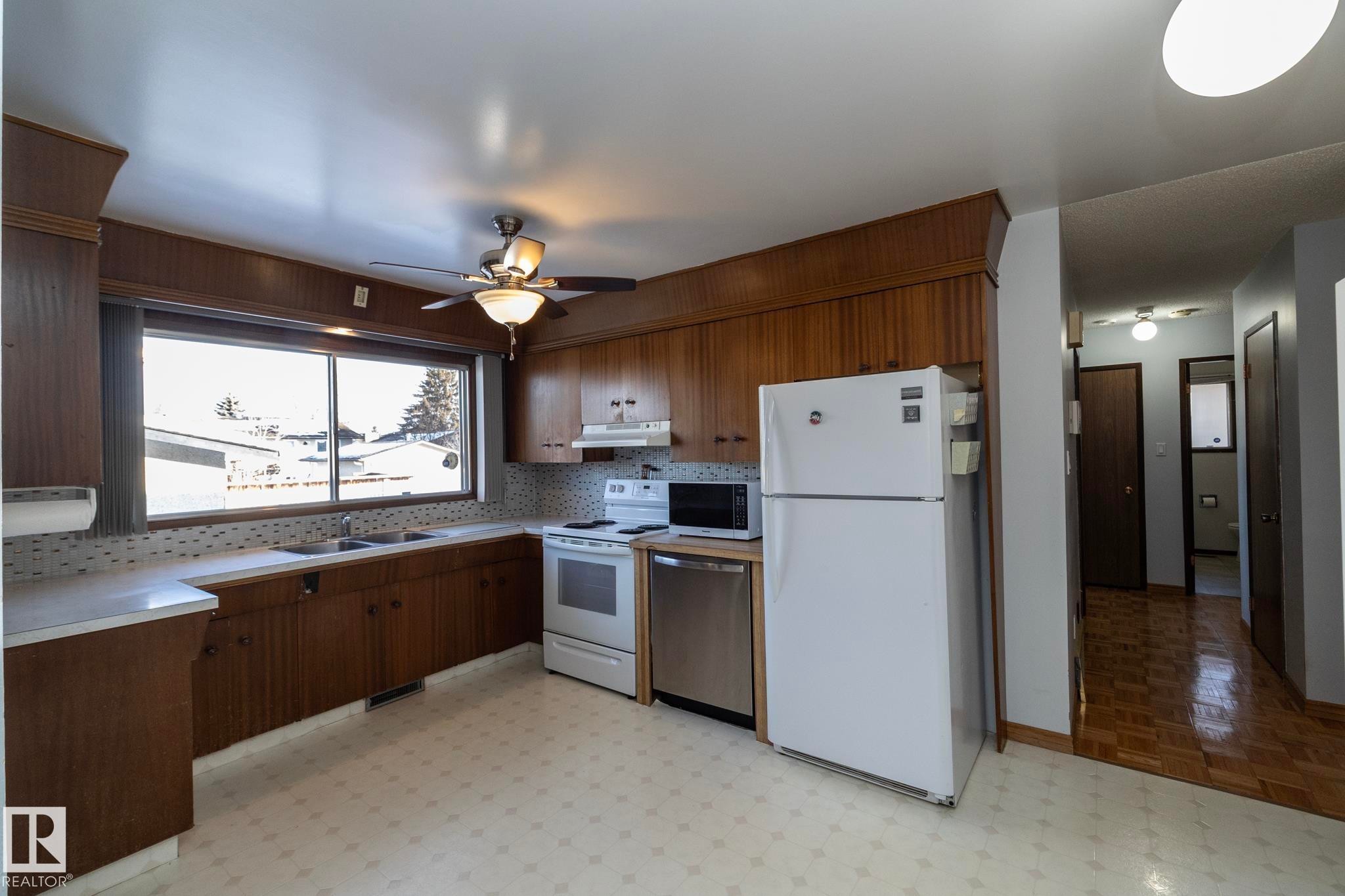 Kitchen with white appliances, light countertops, a ceiling fan, light flooring, and backsplash - 9020 152 Avenue, Edmonton, AB - Indoor Photo Showing Kitchen With Double Sink