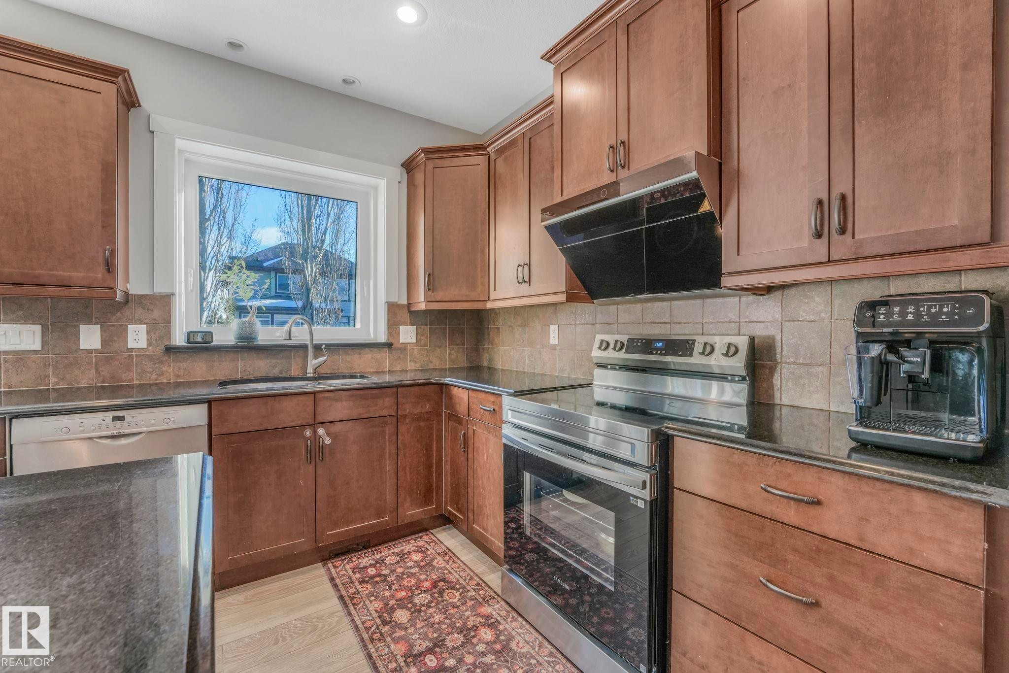 Kitchen featuring appliances with stainless steel finishes, ventilation hood, brown cabinets, decorative backsplash, and recessed lighting - 2307 Rutherford Way, Edmonton, AB - Indoor Photo Showing Kitchen