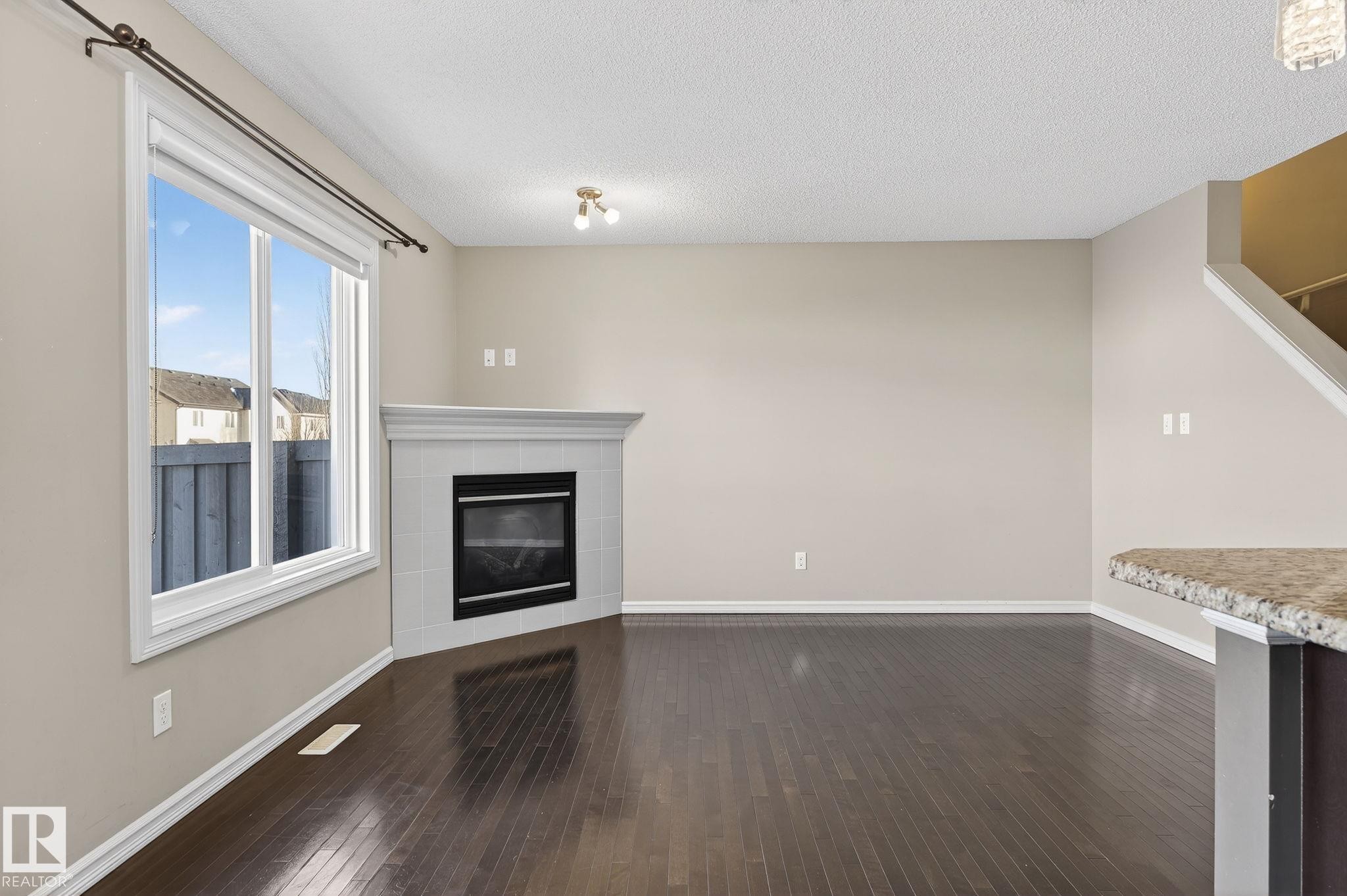 Unfurnished living room with dark wood-style floors, a tiled fireplace, and a textured ceiling - 2338 Casselman Crescent, Edmonton, AB - Indoor With Fireplace