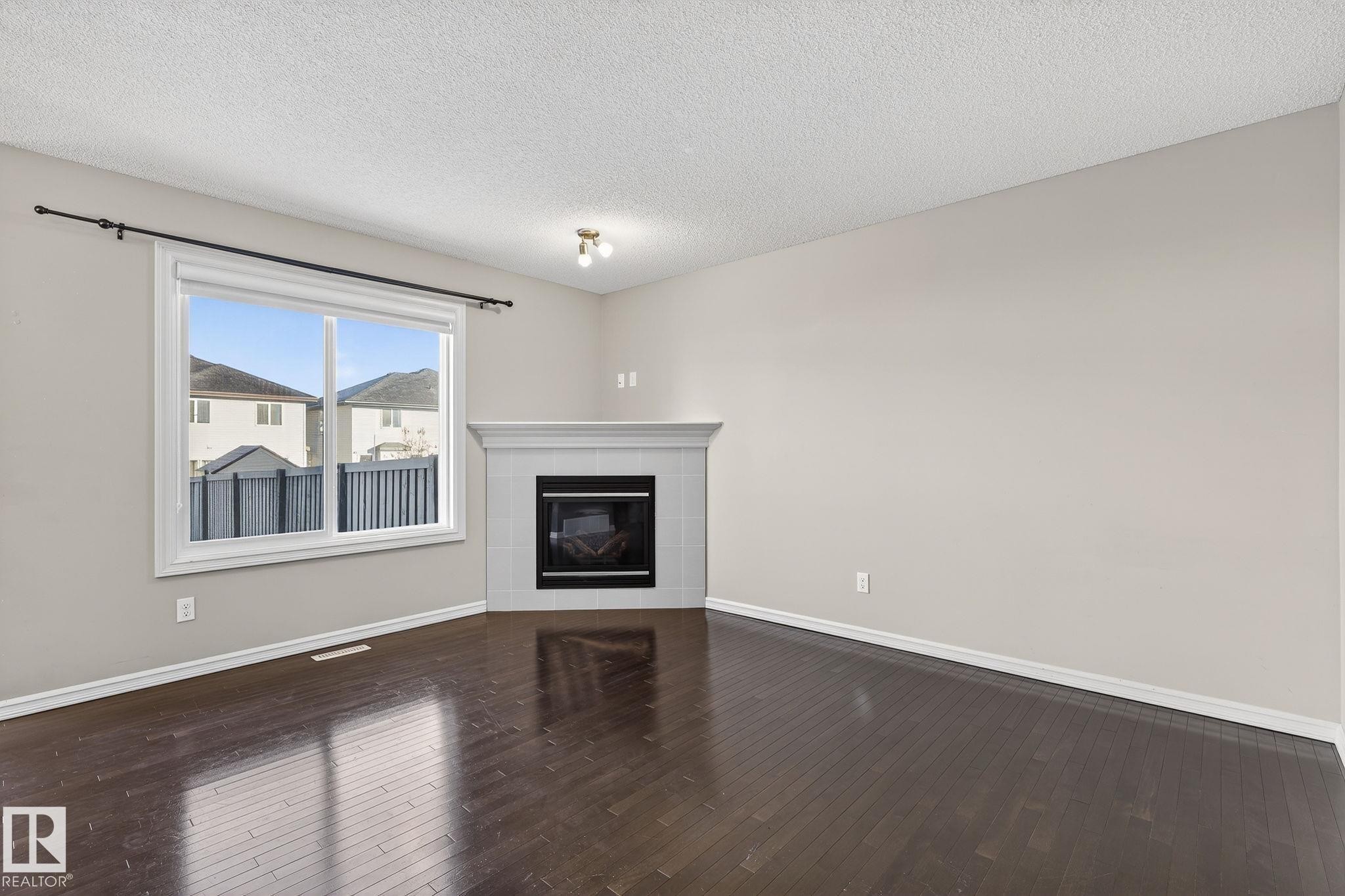 Unfurnished living room featuring dark wood finished floors, a tiled fireplace, and a textured ceiling - 2338 Casselman Crescent, Edmonton, AB - Indoor Photo Showing Living Room With Fireplace