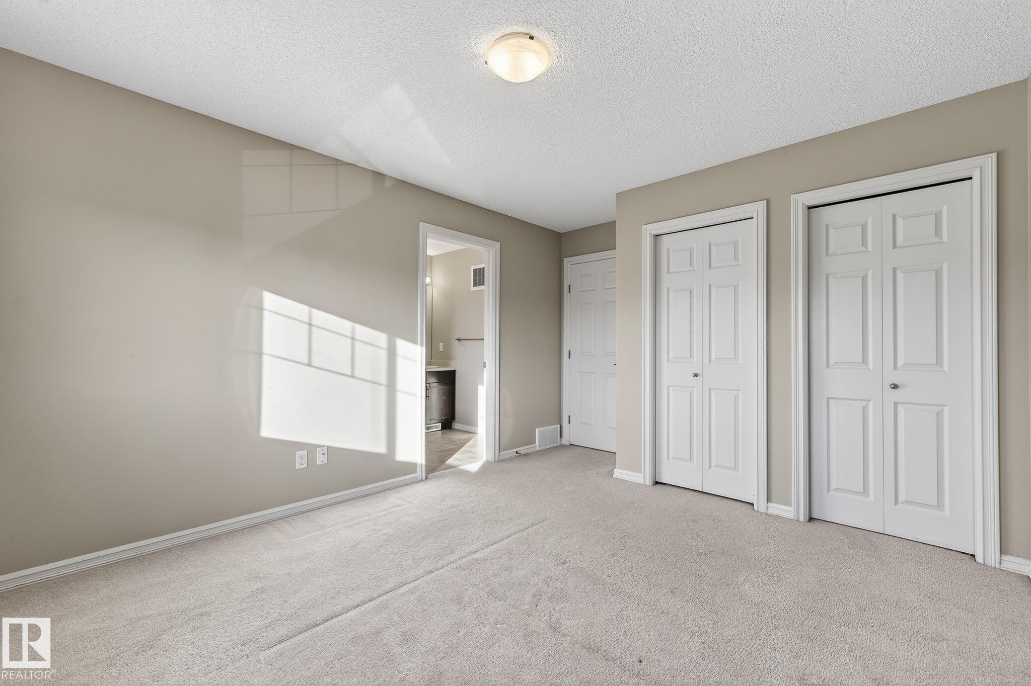 Unfurnished bedroom featuring two closets, carpet floors, ensuite bath, and a textured ceiling - 2338 Casselman Crescent, Edmonton, AB - Indoor
