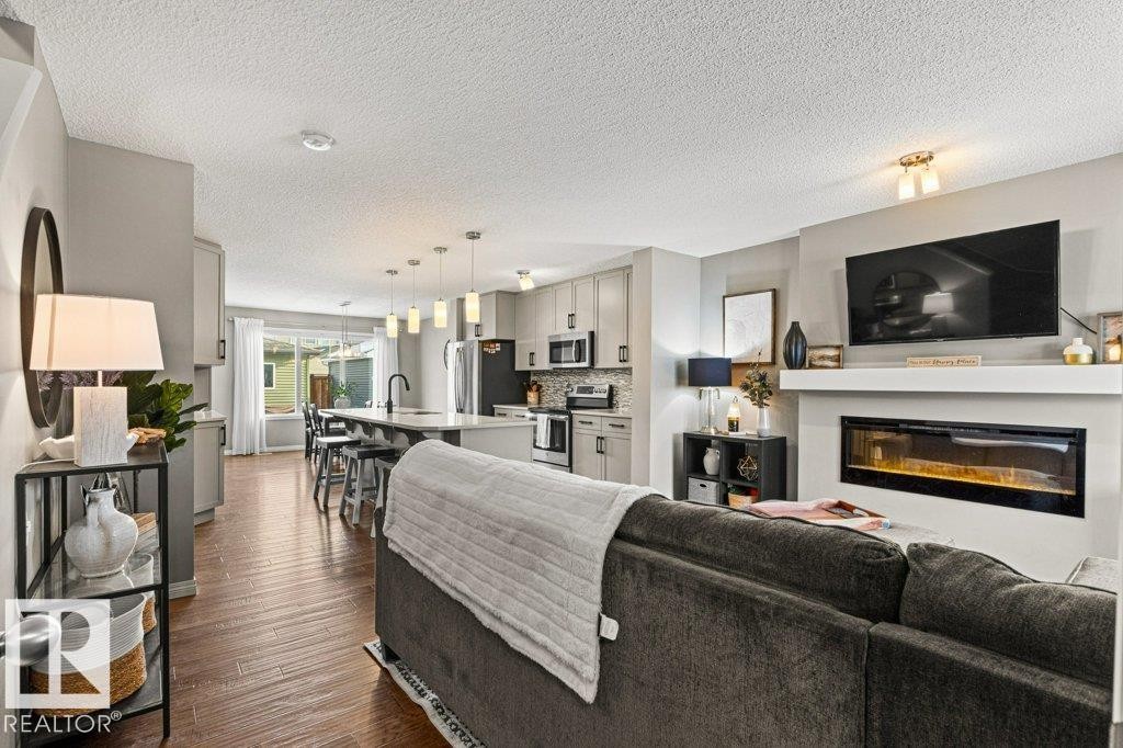 Living room with a glass covered fireplace, dark wood finished floors, and a textured ceiling - 3351 Orchards Link, Edmonton, AB - Indoor Photo Showing Living Room With Fireplace