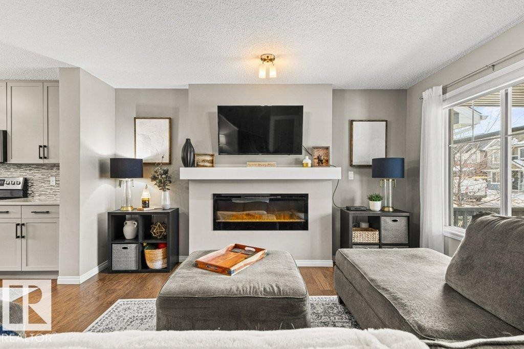 Living room with a glass covered fireplace, dark wood-style flooring, and a textured ceiling - 3351 Orchards Link, Edmonton, AB - Indoor Photo Showing Living Room With Fireplace