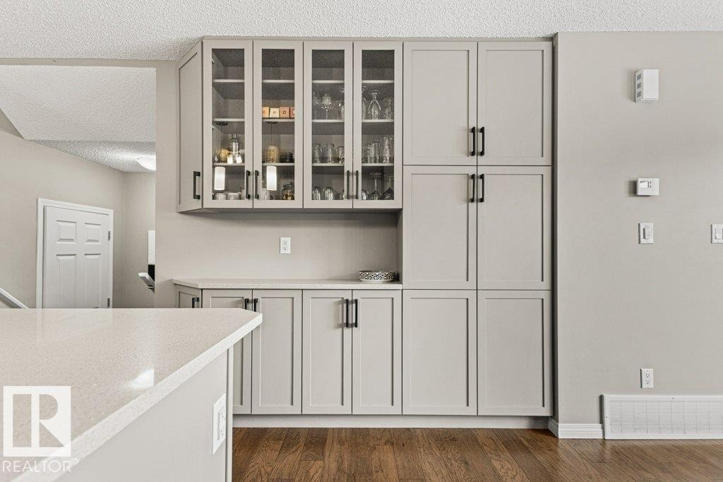 Bar area featuring light stone counters, glass fronted cabinets, dark wood finished floors, a textured ceiling, and gray cabinets - 3351 Orchards Link, Edmonton, AB - Indoor Photo Showing Other Room