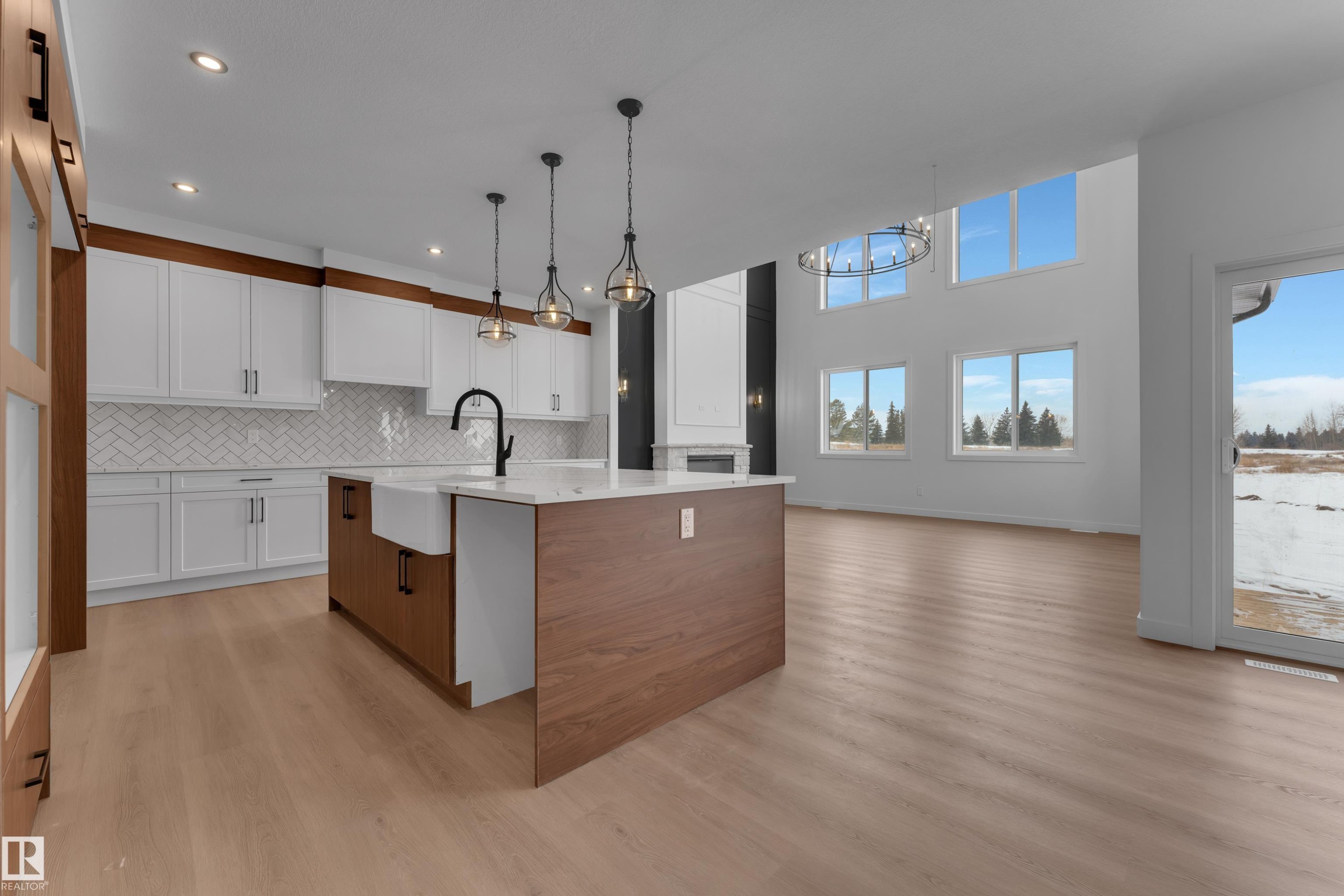 Dual tone kitchen featuring two tone cabinets, a center island with sink, light wood-style floors, open floor plan, and light stone countertops - 40 Grayson Green, Stony Plain, AB - Indoor Photo Showing Kitchen With Upgraded Kitchen