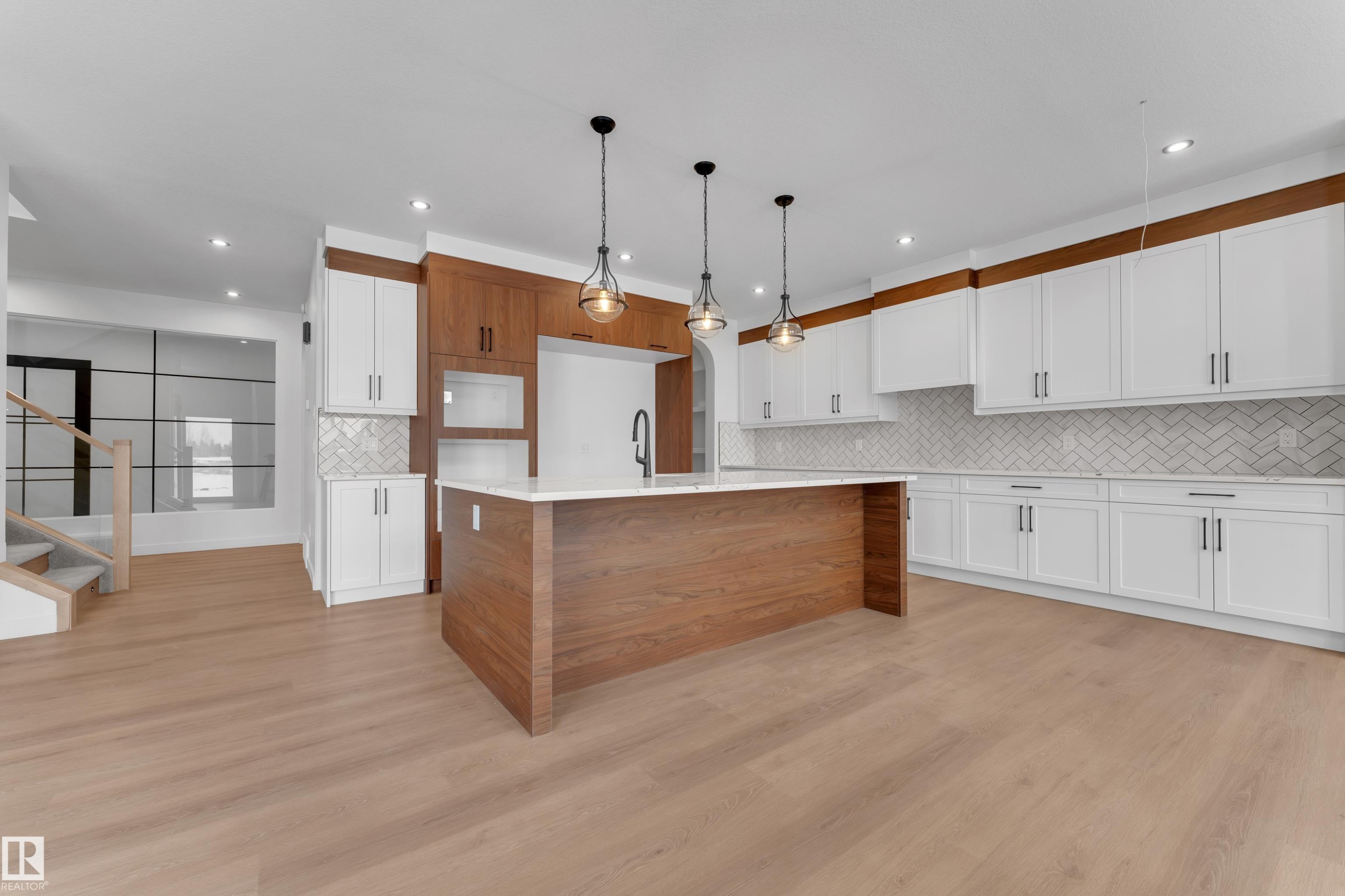 Kitchen with a center island with sink, pendant lighting, dual tone cabinetry, light stone countertops, and light wood-type flooring - 40 Grayson Green, Stony Plain, AB - Indoor Photo Showing Kitchen
