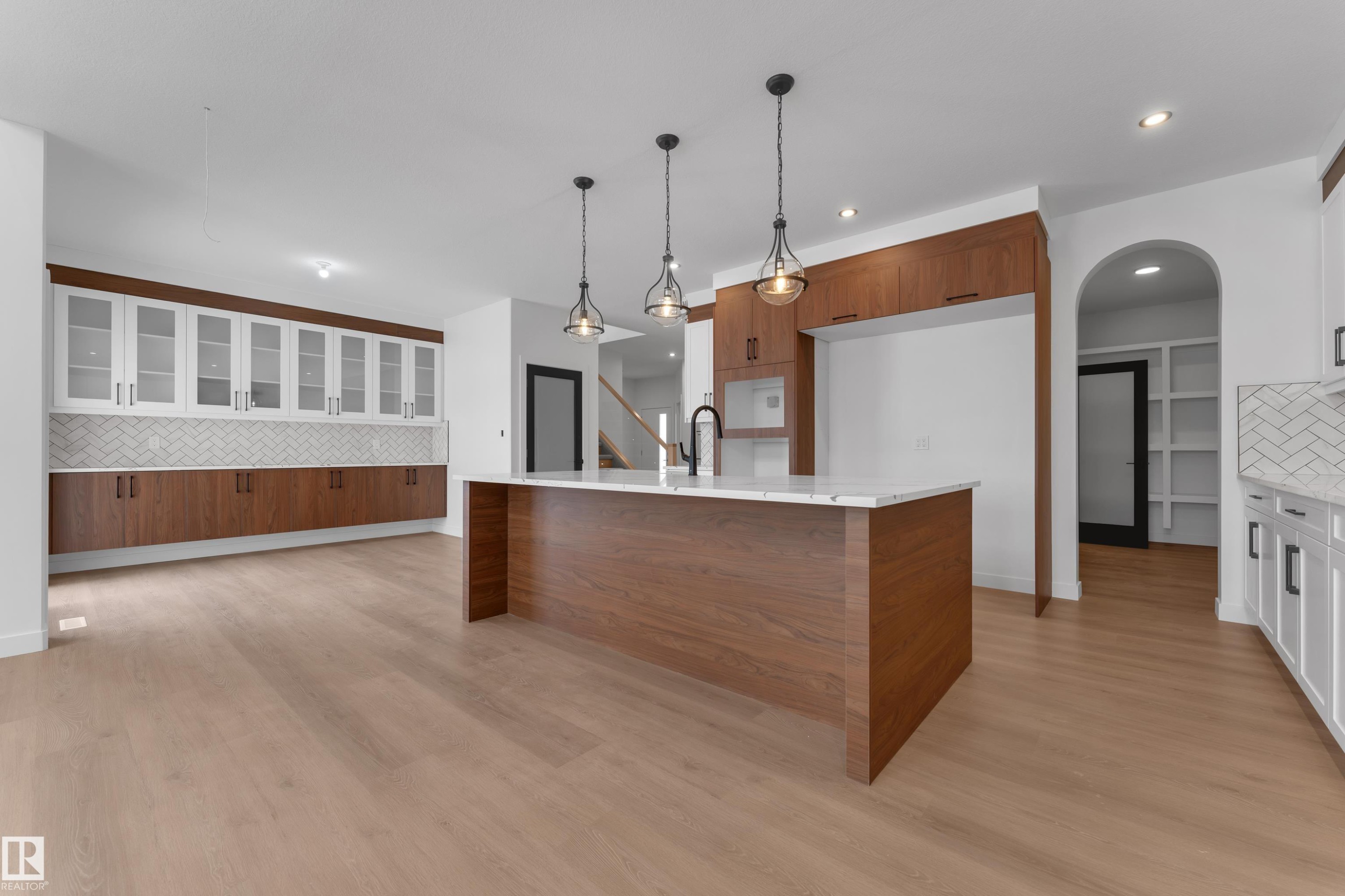 Kitchen with decorative backsplash, arched walkways, light stone counters, hanging light fixtures, and light wood-type flooring - 40 Grayson Green, Stony Plain, AB - Indoor Photo Showing Kitchen With Upgraded Kitchen