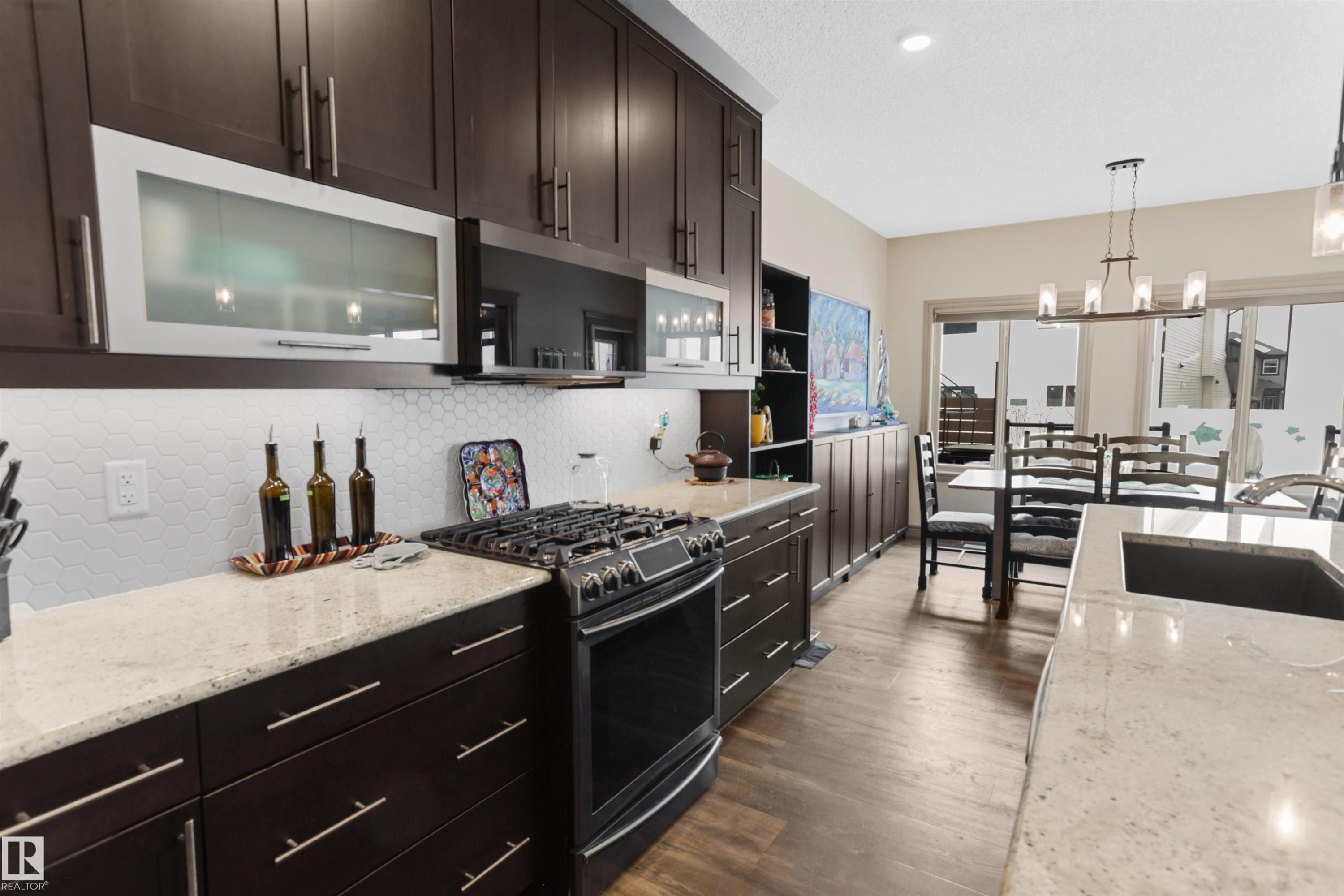 Kitchen featuring light stone countertops, gas stove, dark wood finish cabinetry, tasteful backsplash, and hanging lights - 97 Astoria Point(E), Devon, AB - Indoor Photo Showing Kitchen With Upgraded Kitchen