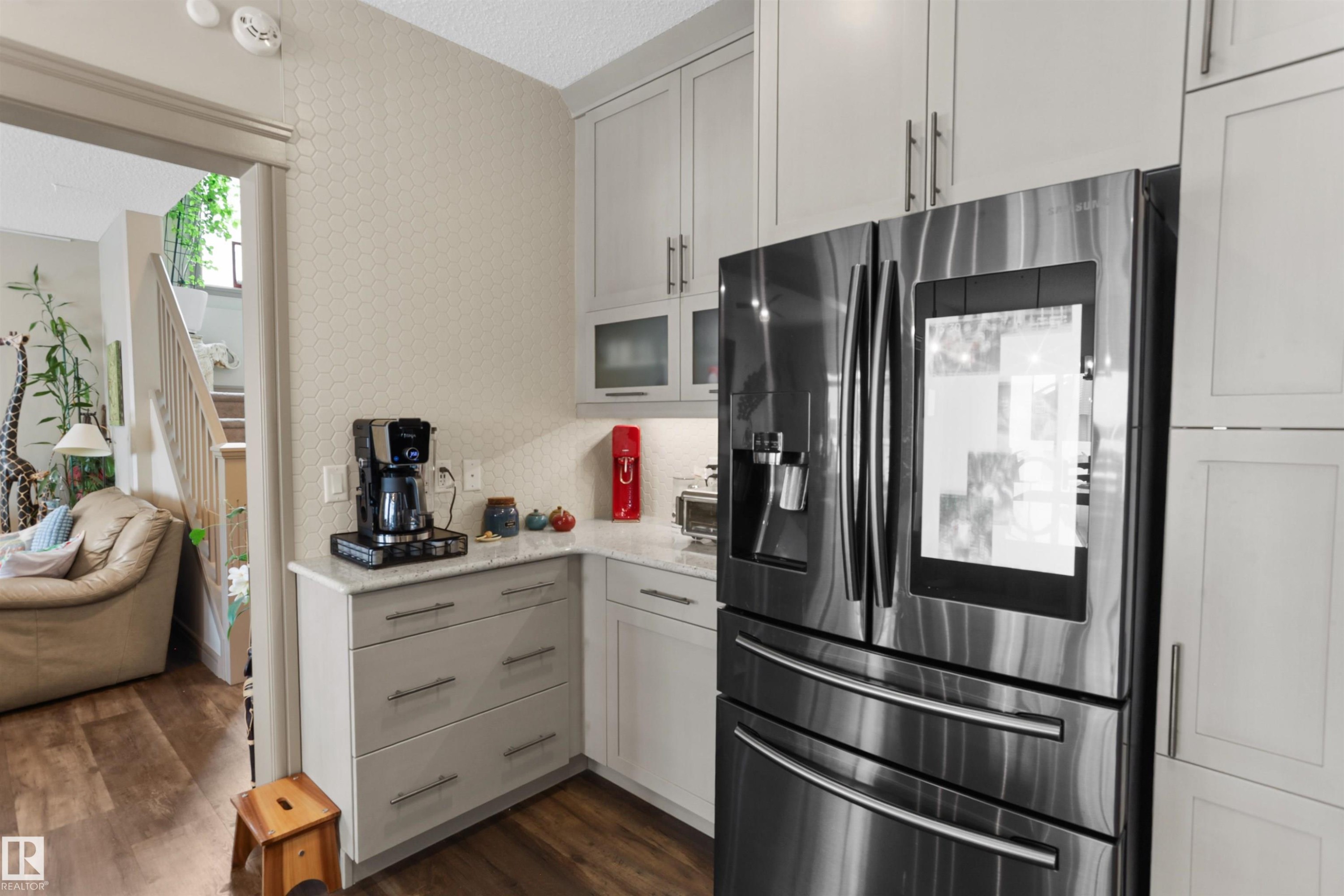Kitchen with stainless steel refrigerator with ice dispenser, dark wood-style flooring, light stone counters, glass insert cabinets, and open floor plan - 97 Astoria Point(E), Devon, AB - Indoor Photo Showing Kitchen
