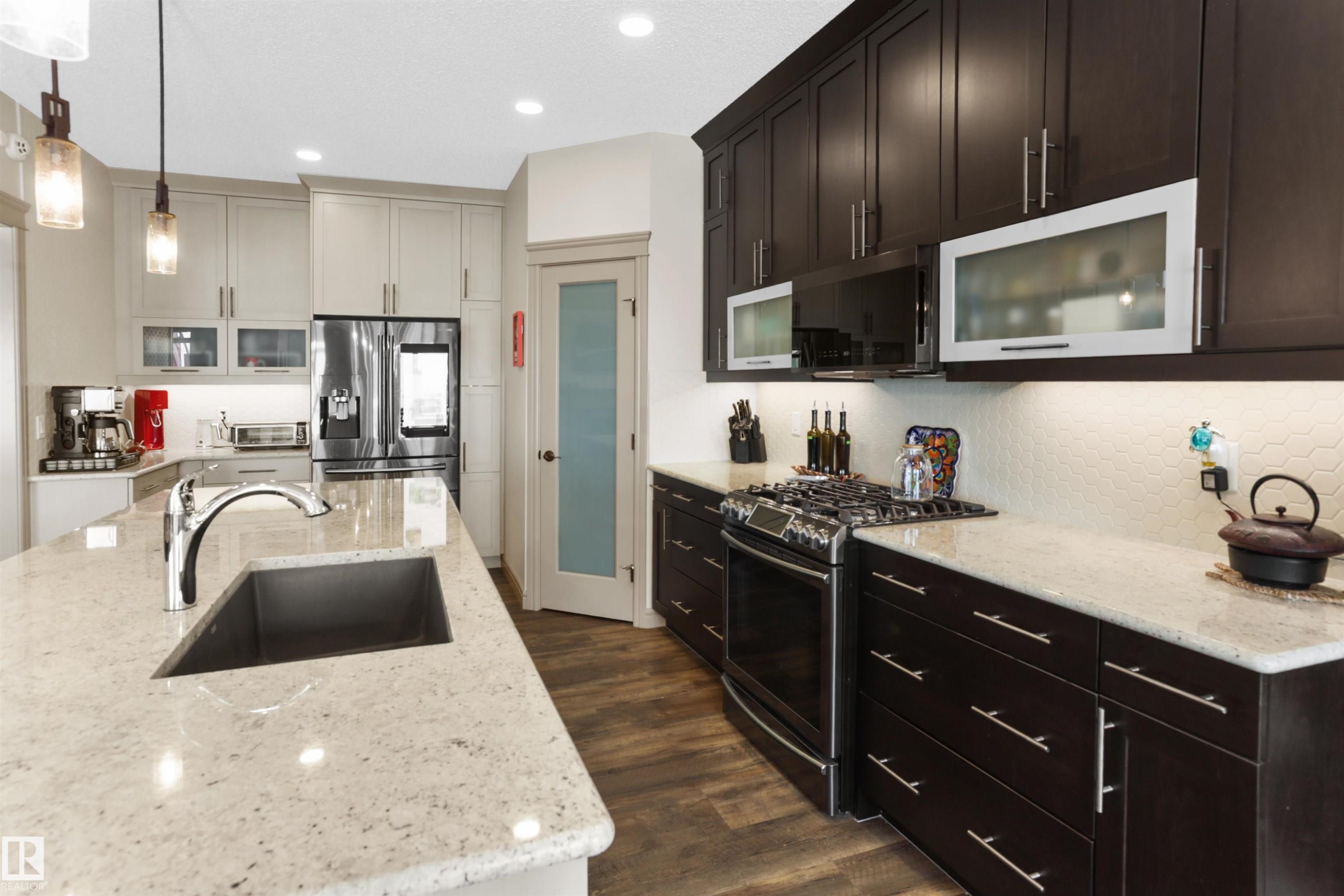 Kitchen with stainless steel appliances, light stone countertops, glass fronted cabinets, and hanging light fixtures - 97 Astoria Point(E), Devon, AB - Indoor Photo Showing Kitchen With Upgraded Kitchen