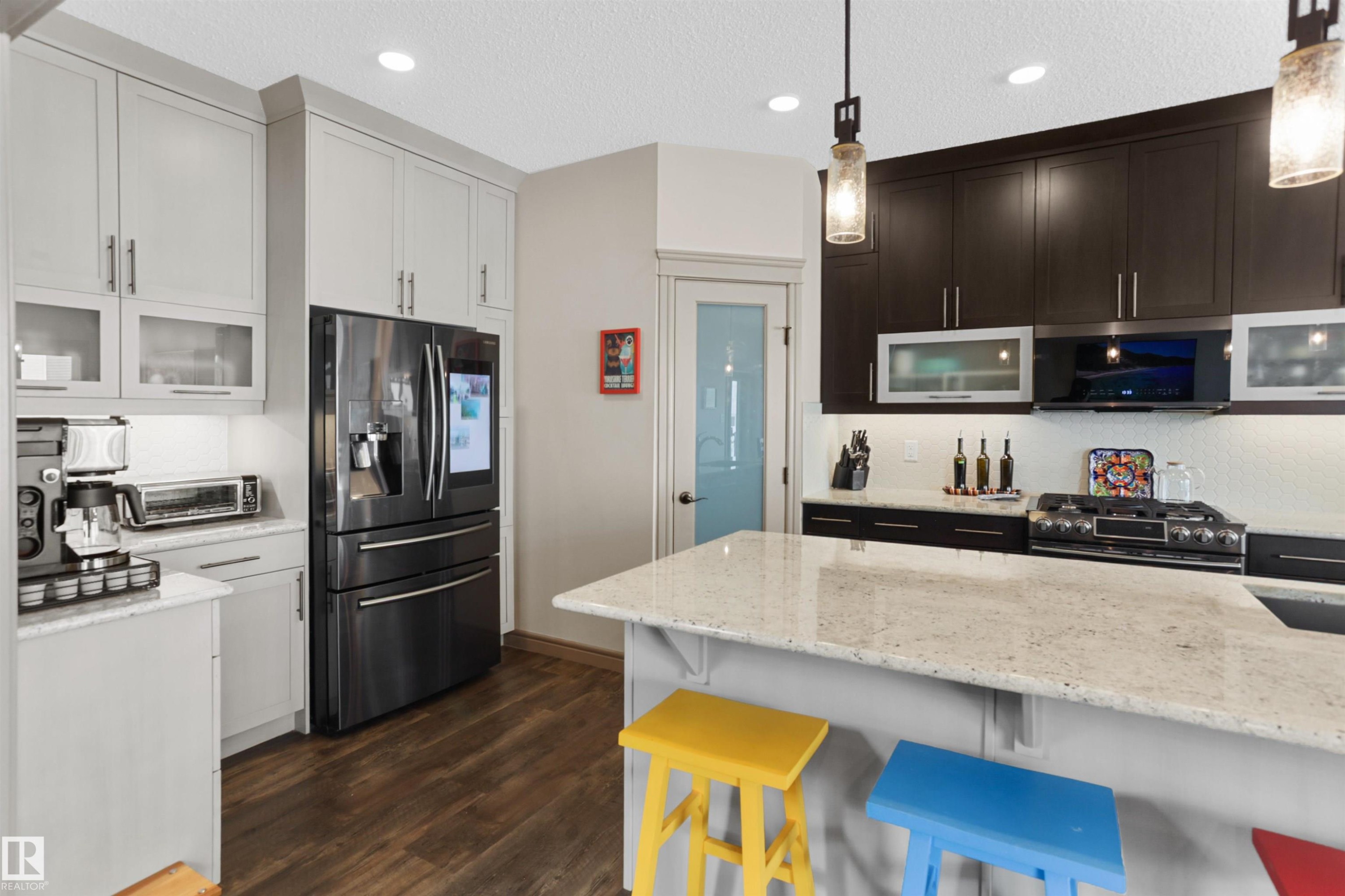 Kitchen with glass fronted cabinets, stainless steel appliances, light stone counters, hanging light fixtures, and a textured ceiling - 97 Astoria Point(E), Devon, AB - Indoor Photo Showing Kitchen With Upgraded Kitchen