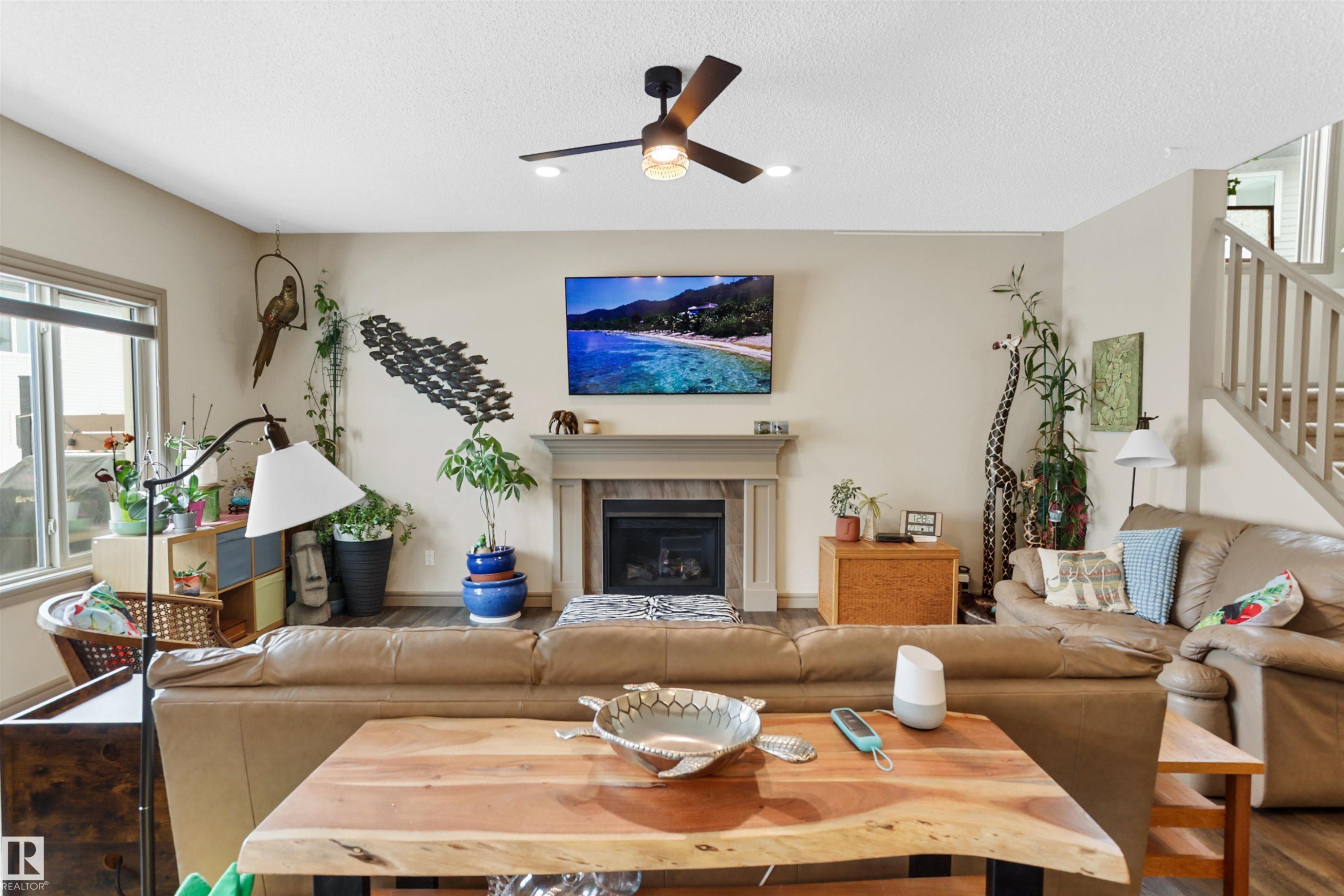 Living area with ceiling fan, wood finished floors, a tile fireplace, and a textured ceiling - 97 Astoria Point(E), Devon, AB - Indoor Photo Showing Living Room With Fireplace