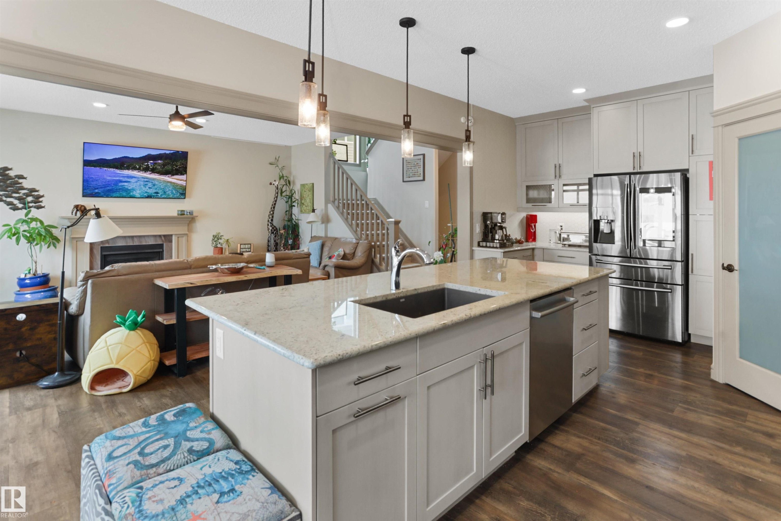 Kitchen featuring stainless steel appliances, a ceiling fan, a fireplace, decorative light fixtures, and light stone counters - 97 Astoria Point(E), Devon, AB - Indoor Photo Showing Kitchen With Upgraded Kitchen