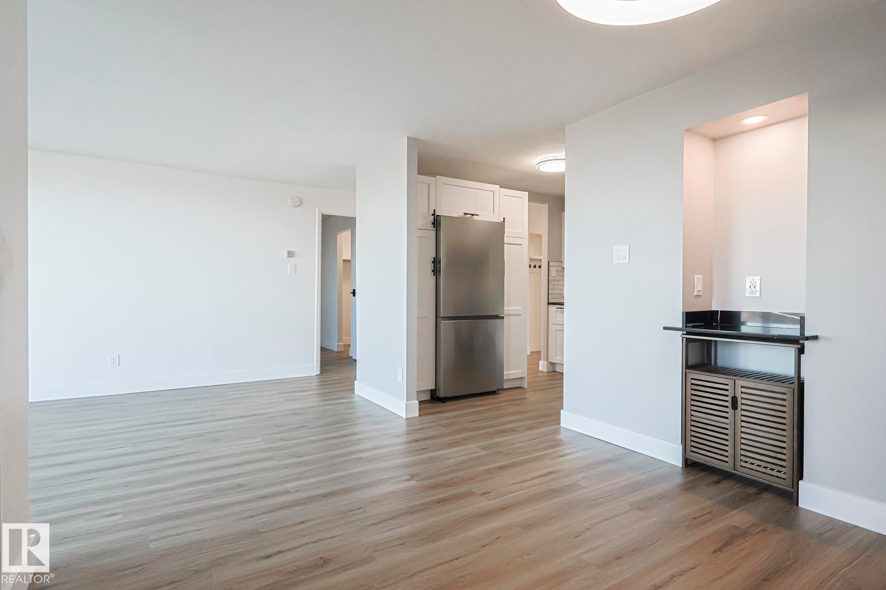 Unfurnished living room featuring light wood-style vinyl plank floors and baseboards - 505 10149 Saskatchewan Drive, Edmonton, AB - Indoor Photo Showing Kitchen
