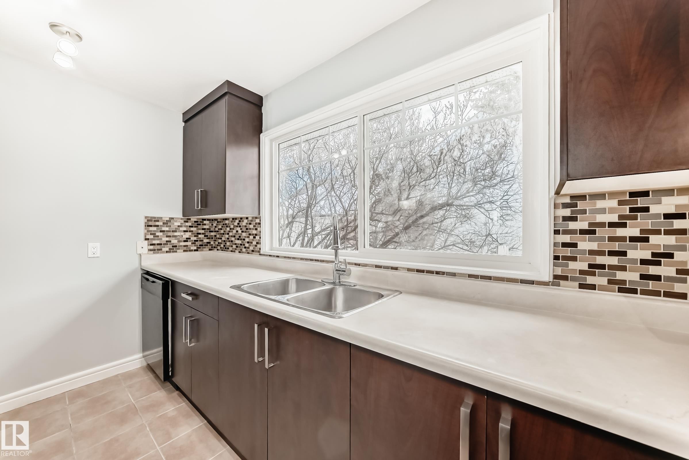 Kitchen featuring backsplash, light countertops, dark brown cabinetry, and stainless steel dishwasher - 10331 153 Street, Edmonton, AB - Indoor Photo Showing Kitchen With Double Sink