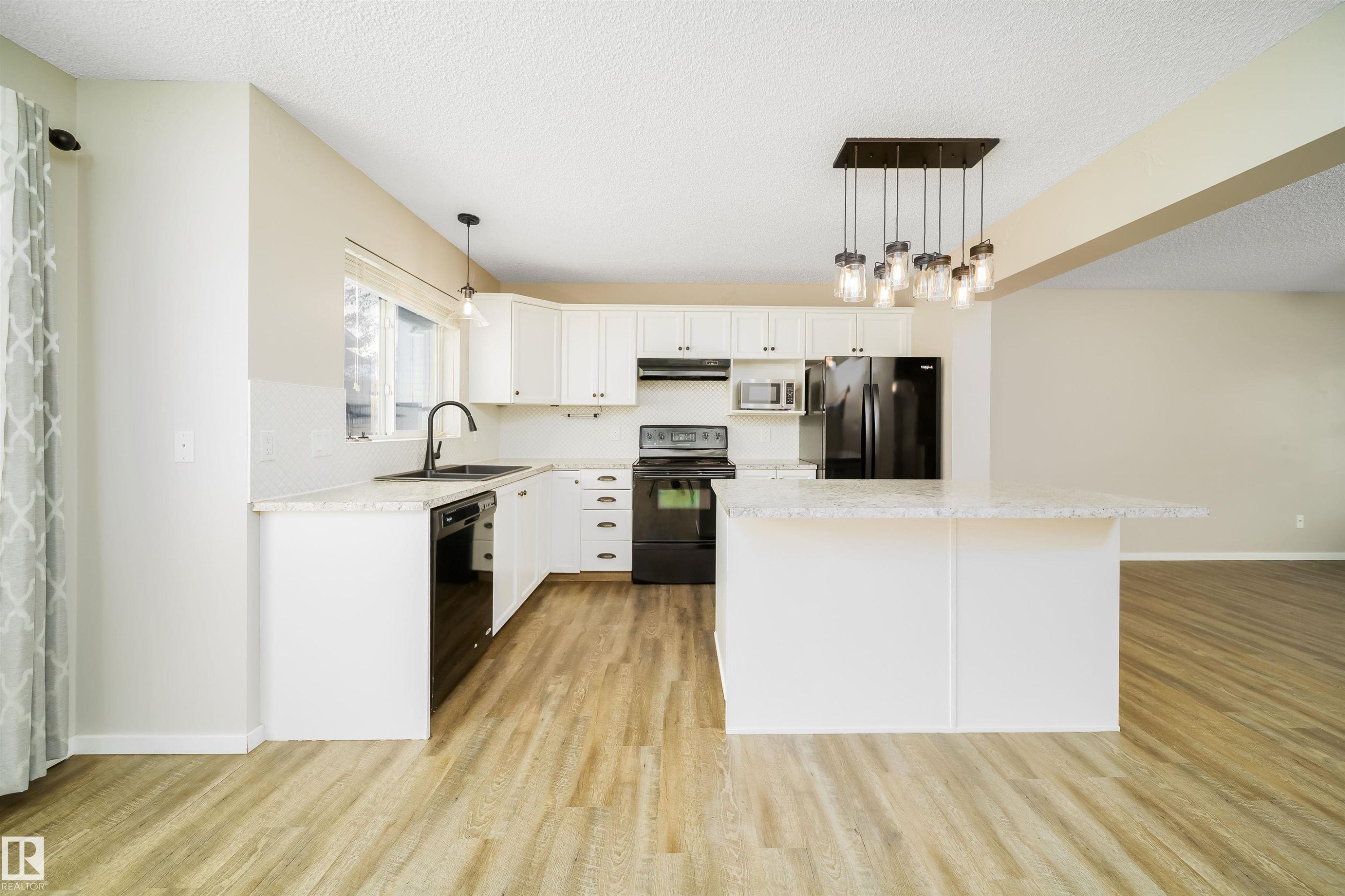 Kitchen featuring pendant lighting, white cabinets, black appliances, a textured ceiling, and a center island - 1695 Tompkins Place, Edmonton, AB - Indoor Photo Showing Kitchen