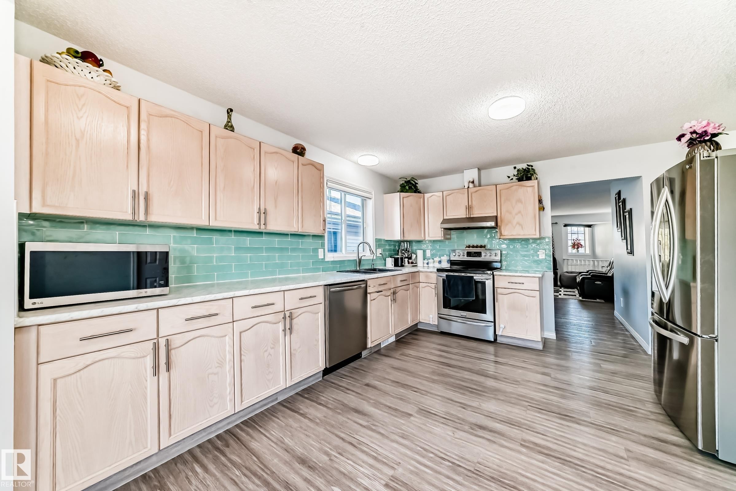 Kitchen featuring light wood finish cabinetry, stainless steel appliances, light wood-style floors, a textured ceiling, and tasteful backsplash - 6 Jefferson Road, Edmonton, AB - Indoor Photo Showing Kitchen