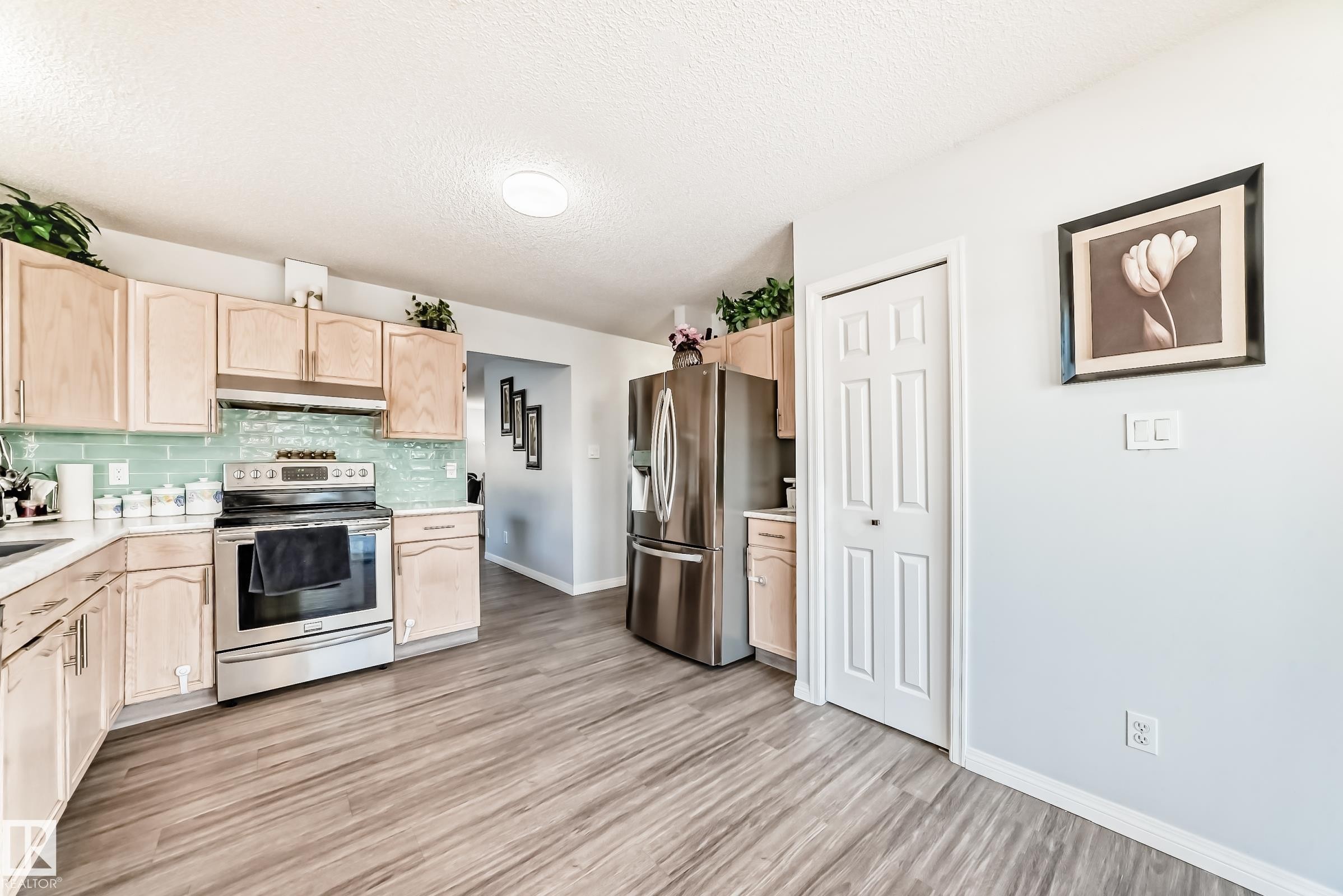 Kitchen with light wood finish cabinetry, stainless steel appliances, decorative backsplash, light wood finished floors, and a textured ceiling - 6 Jefferson Road, Edmonton, AB - Indoor Photo Showing Kitchen