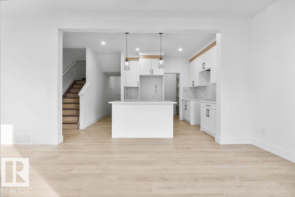 Kitchen with white cabinetry, a center island with sink, pendant lighting, light wood-type flooring, and light stone counters - 235 Linden Loop, Leduc, AB - Indoor Photo Showing Kitchen