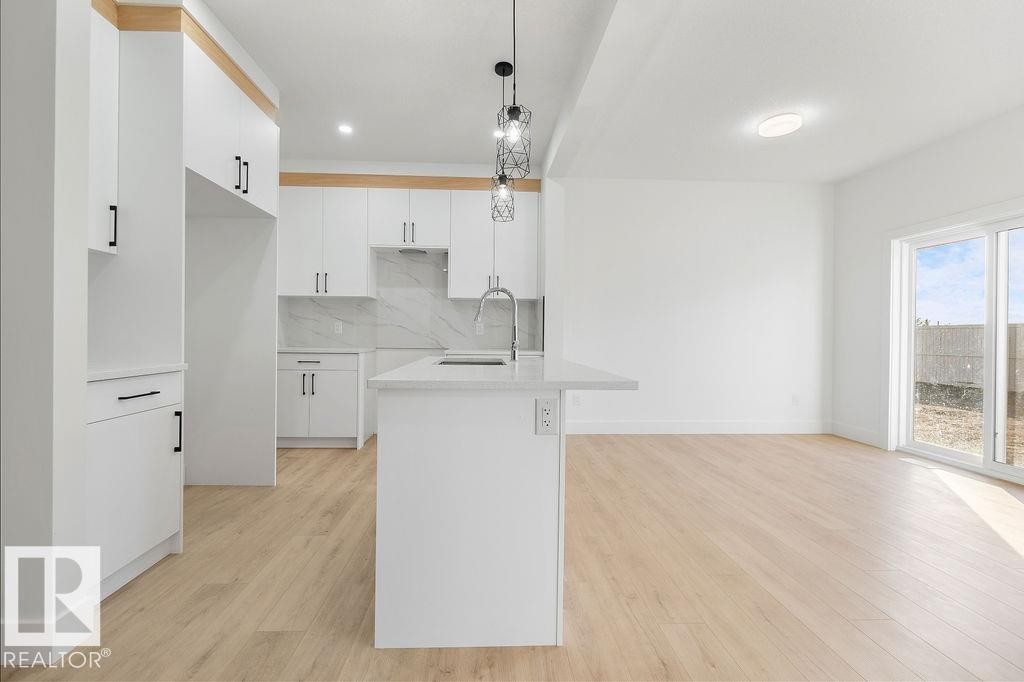Kitchen featuring white cabinets, tasteful backsplash, light wood-type flooring, pendant lighting, and light stone counters - 235 Linden Loop, Leduc, AB - Indoor Photo Showing Kitchen