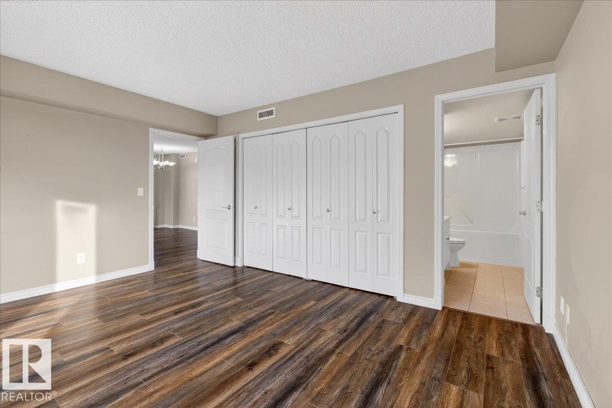 Unfurnished bedroom with wood finished floors, a textured ceiling, a closet, and suspended lighting - 402 10649 Saskatchewan Drive, Edmonton, AB - Indoor Photo Showing Other Room