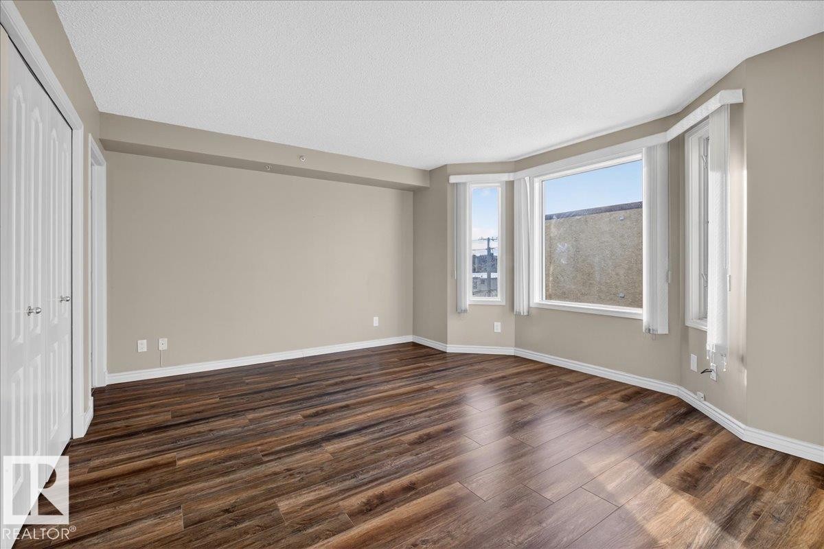 Unfurnished bedroom with a closet, dark wood-style flooring, and a textured ceiling - 402 10649 Saskatchewan Drive, Edmonton, AB - Indoor Photo Showing Other Room