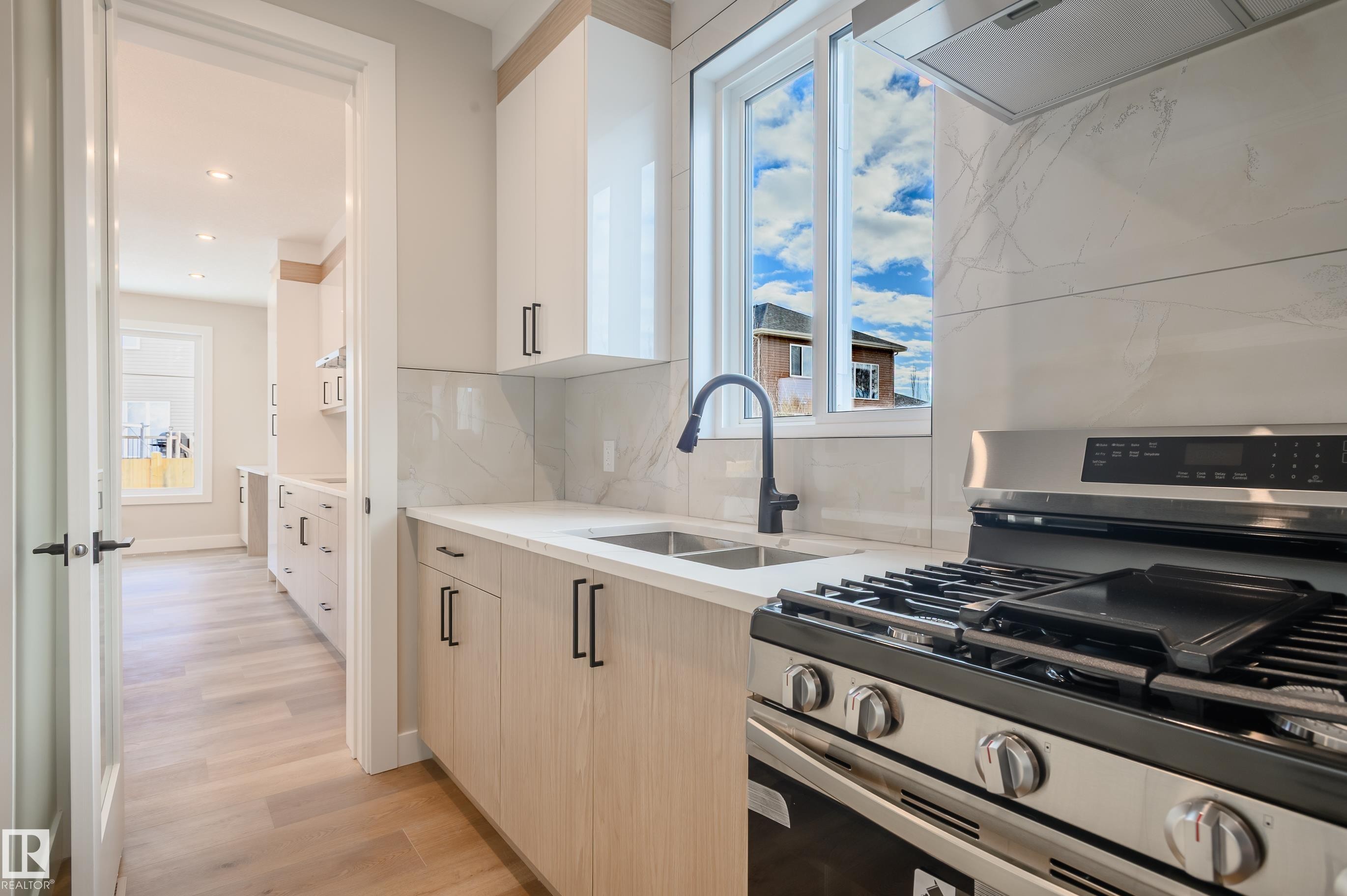 Kitchen featuring stainless steel gas range oven, exhaust hood, light wood-type flooring, light stone countertops, and tasteful backsplash - 16 Middleton Close, Leduc, AB - Indoor Photo Showing Kitchen With Double Sink With Upgraded Kitchen