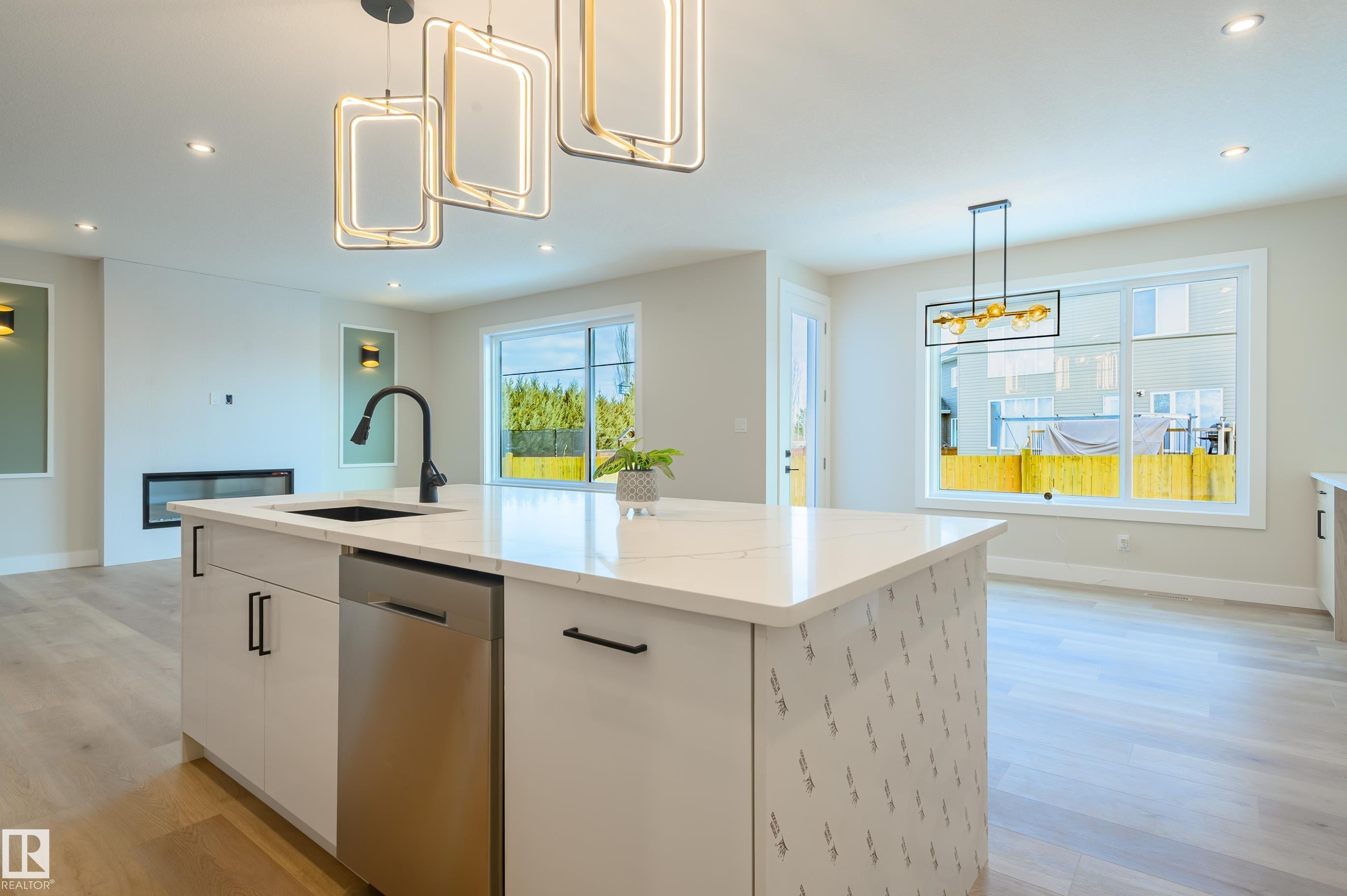 Kitchen featuring white cabinetry, dishwasher, a kitchen island with sink, light wood finished floors, and light stone counters - 16 Middleton Close, Leduc, AB - Indoor Photo Showing Kitchen With Upgraded Kitchen