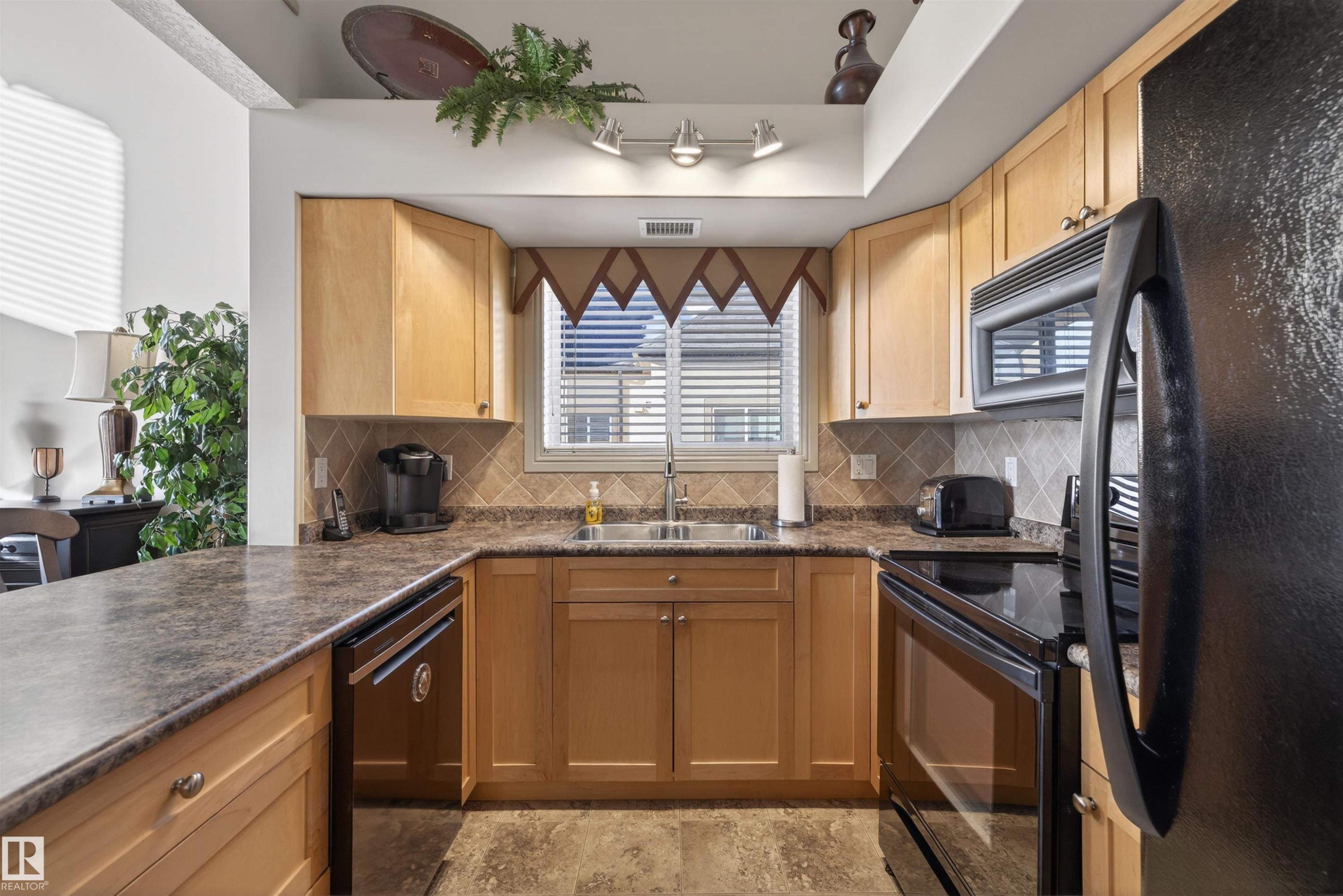Kitchen featuring black appliances, tasteful backsplash, and light stone finish flooring - 427 13005 140 Avenue, Edmonton, AB - Indoor Photo Showing Kitchen With Double Sink