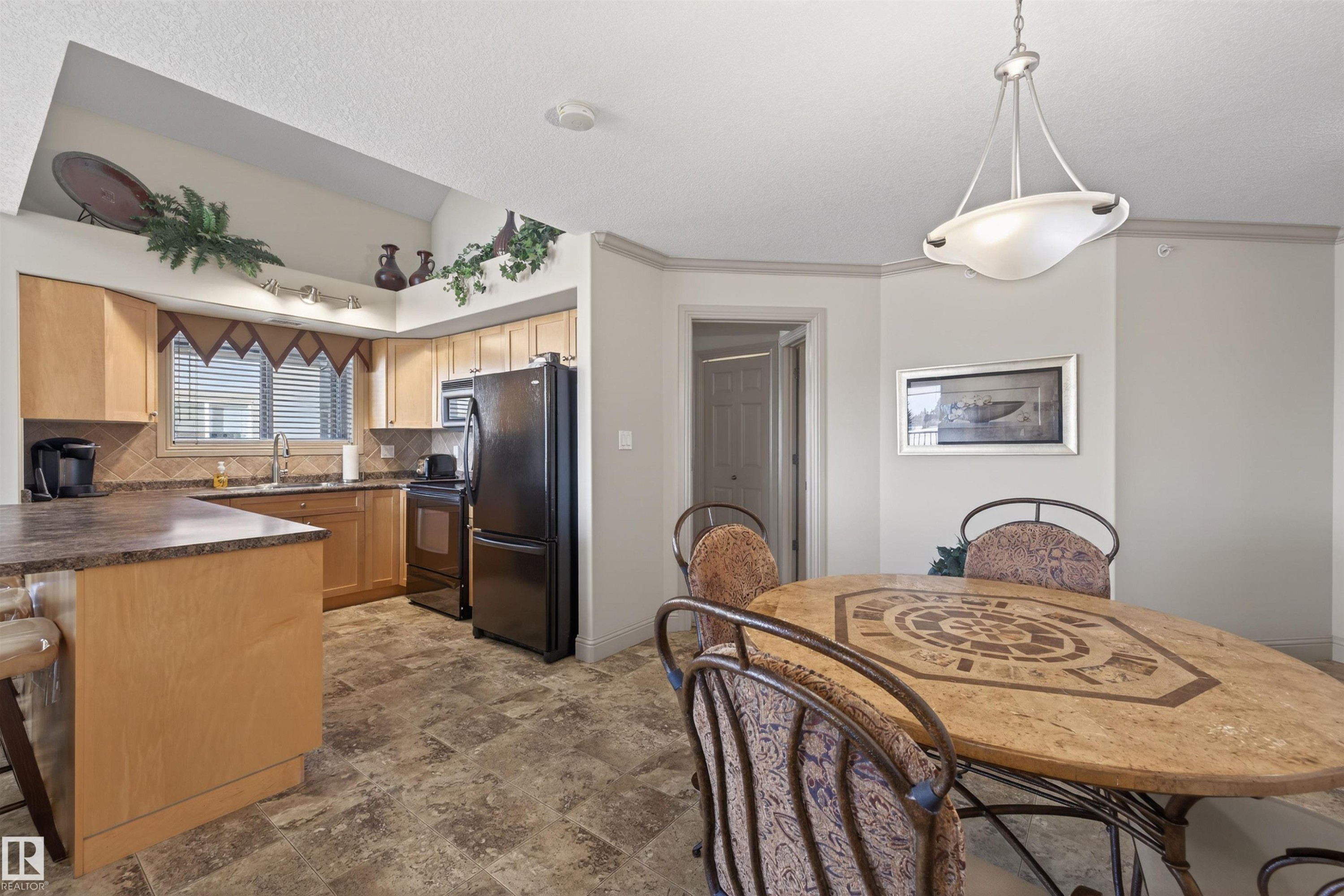 Kitchen featuring black appliances, dark countertops, pendant lighting, ornamental molding, and stone finish flooring - 427 13005 140 Avenue, Edmonton, AB - Indoor
