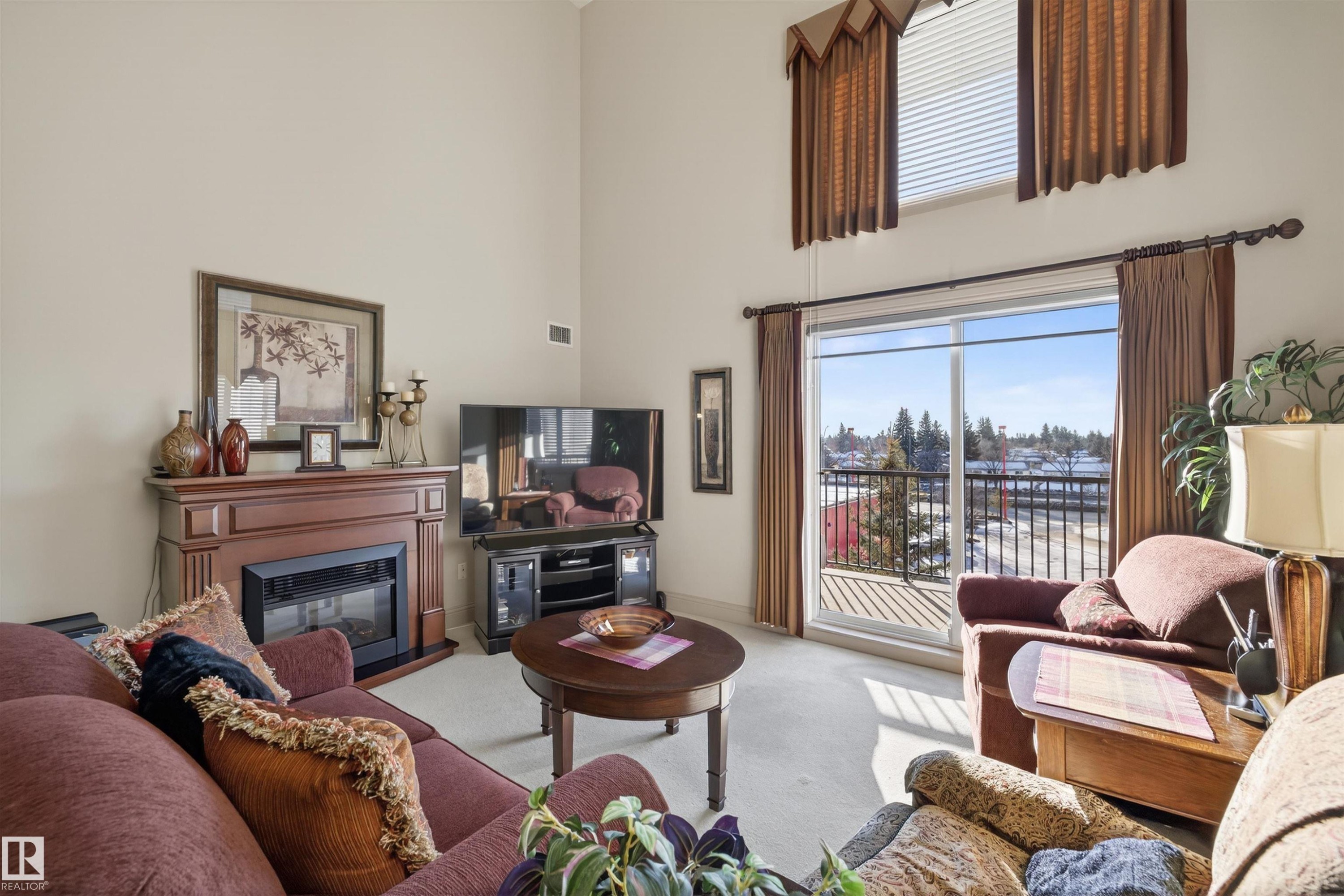 Living area with carpet floors, a glass covered fireplace, and a high ceiling - 427 13005 140 Avenue, Edmonton, AB - Indoor Photo Showing Living Room With Fireplace