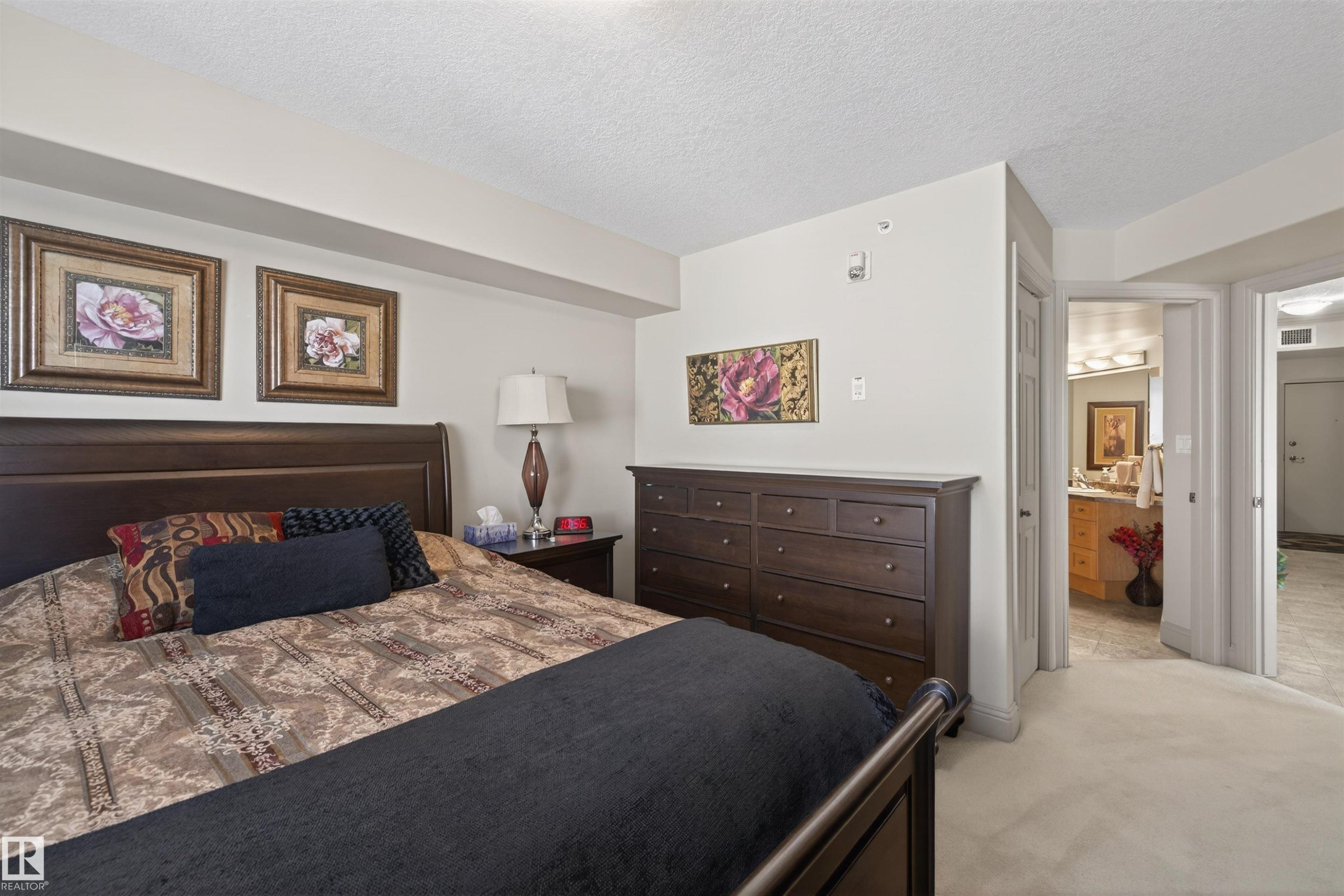 Bedroom featuring a closet, a textured ceiling, light carpet, and connected bathroom - 427 13005 140 Avenue, Edmonton, AB - Indoor Photo Showing Bedroom
