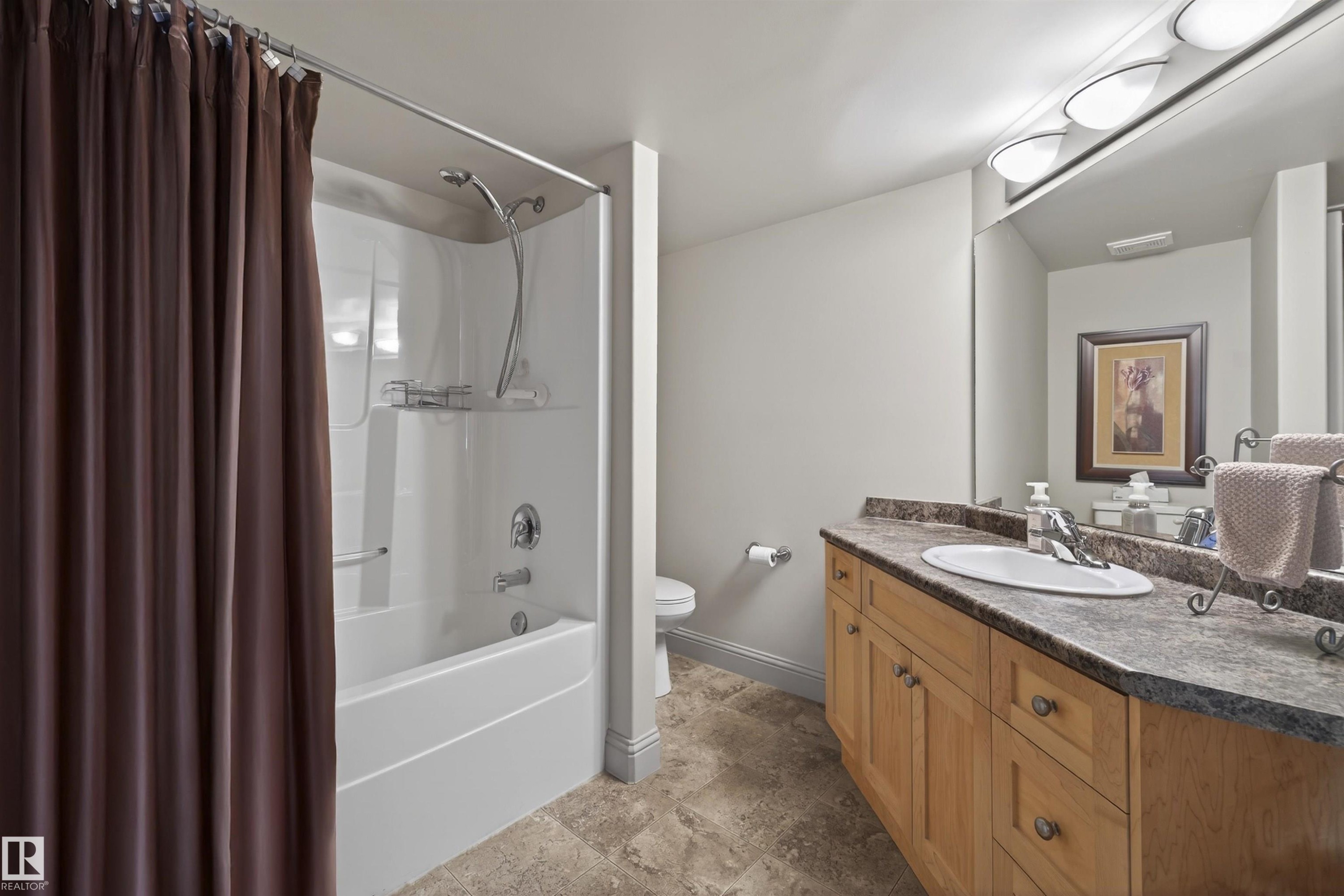 Bathroom with shower / bath combo, vanity, and stone finish floors - 427 13005 140 Avenue, Edmonton, AB - Indoor Photo Showing Bathroom