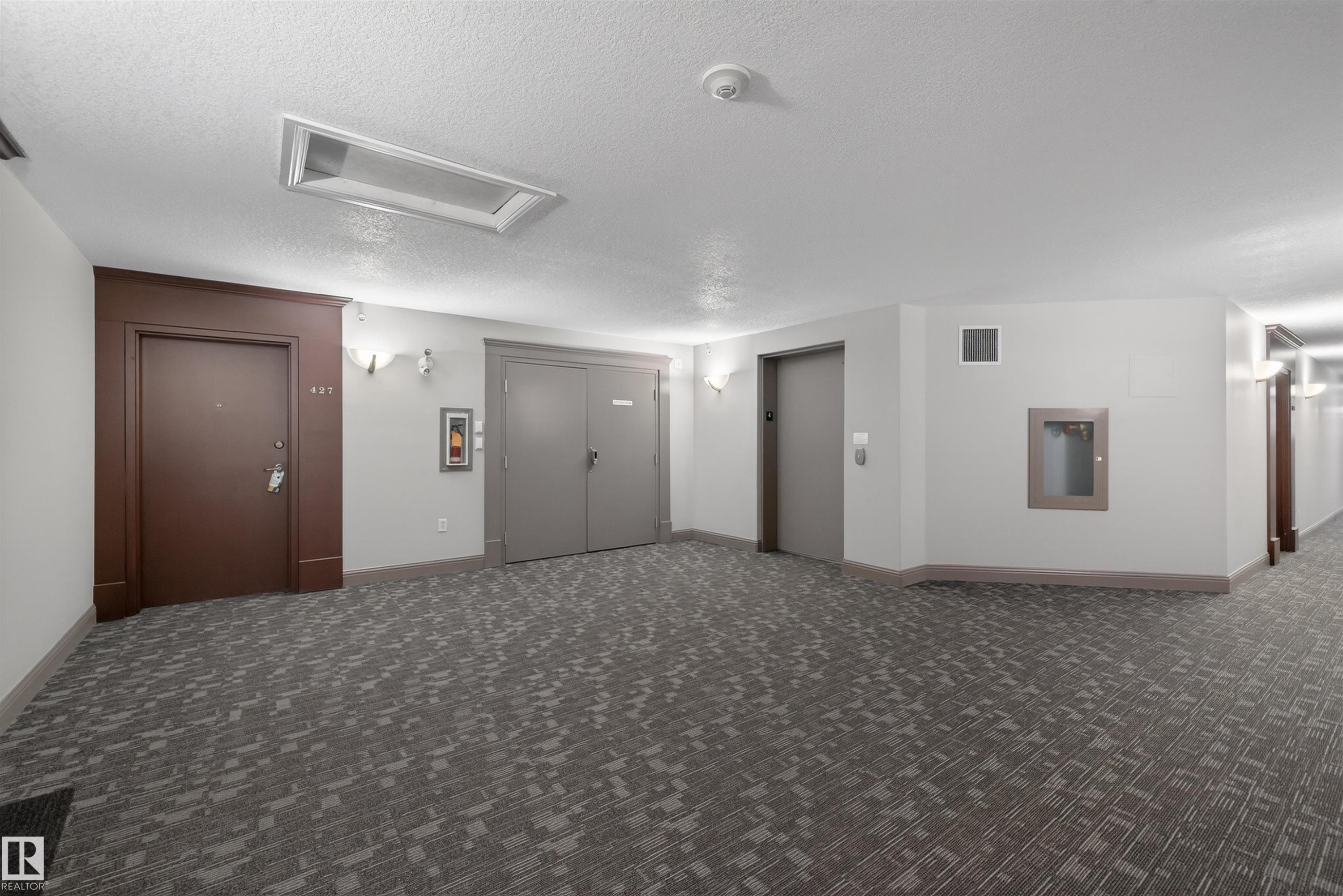Spare room featuring elevator, a textured ceiling, and dark carpet - 427 13005 140 Avenue, Edmonton, AB - Indoor Photo Showing Other Room