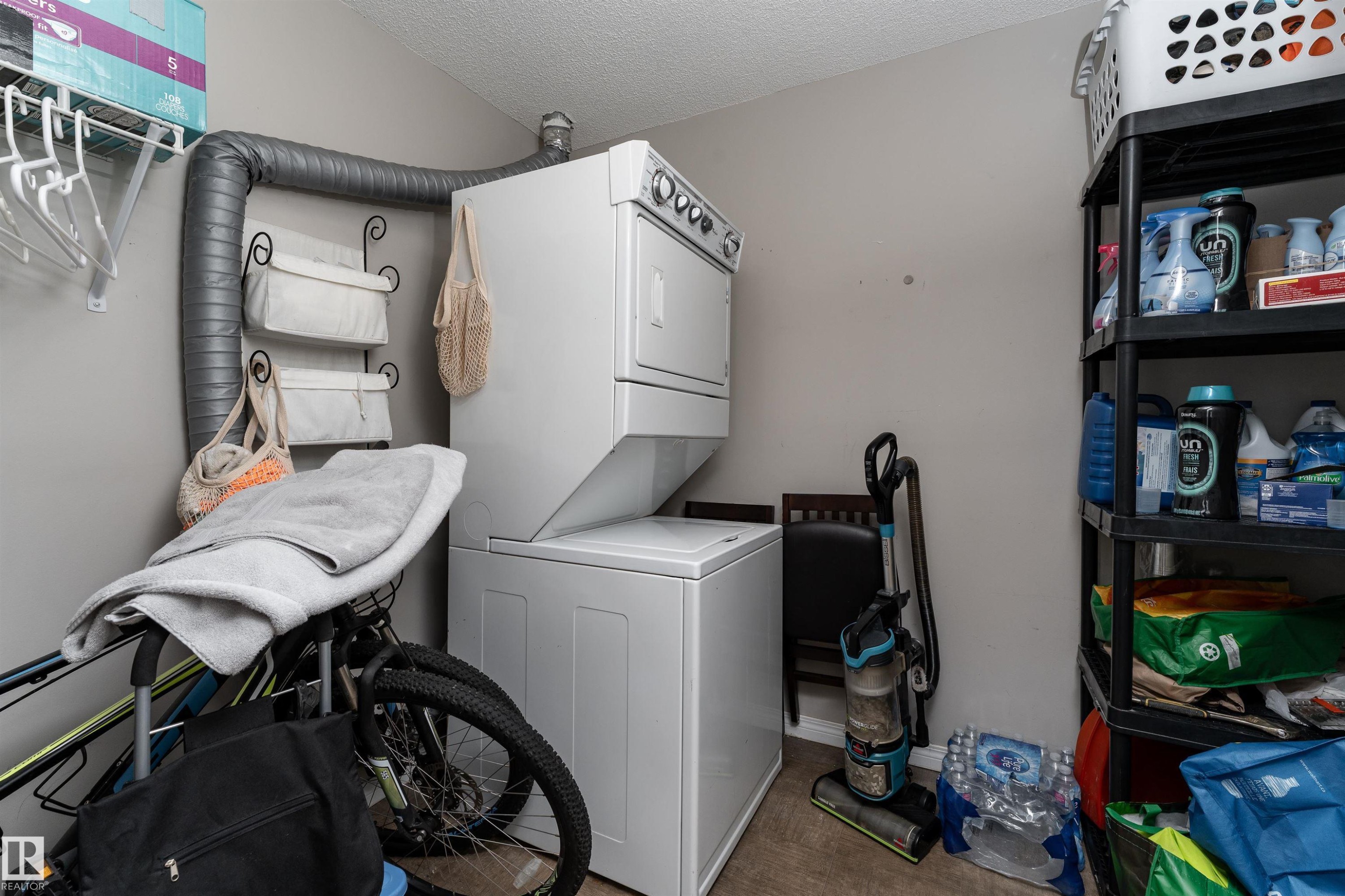 Laundry area featuring stacked washer / dryer, a textured ceiling, parquet floors, and a baseboard heating unit - 325 1520 Hammond Gate, Edmonton, AB - Indoor Photo Showing Laundry Room